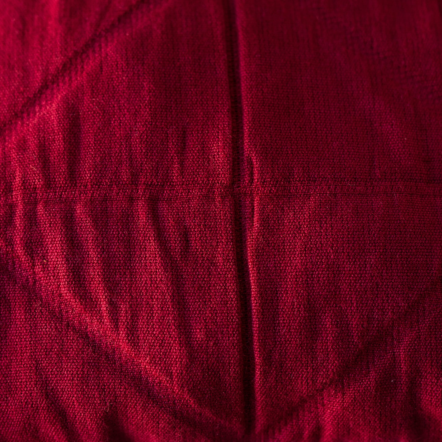A close-up of a deep red quilted fabric with stitched diamond patterns and a central vertical seam.