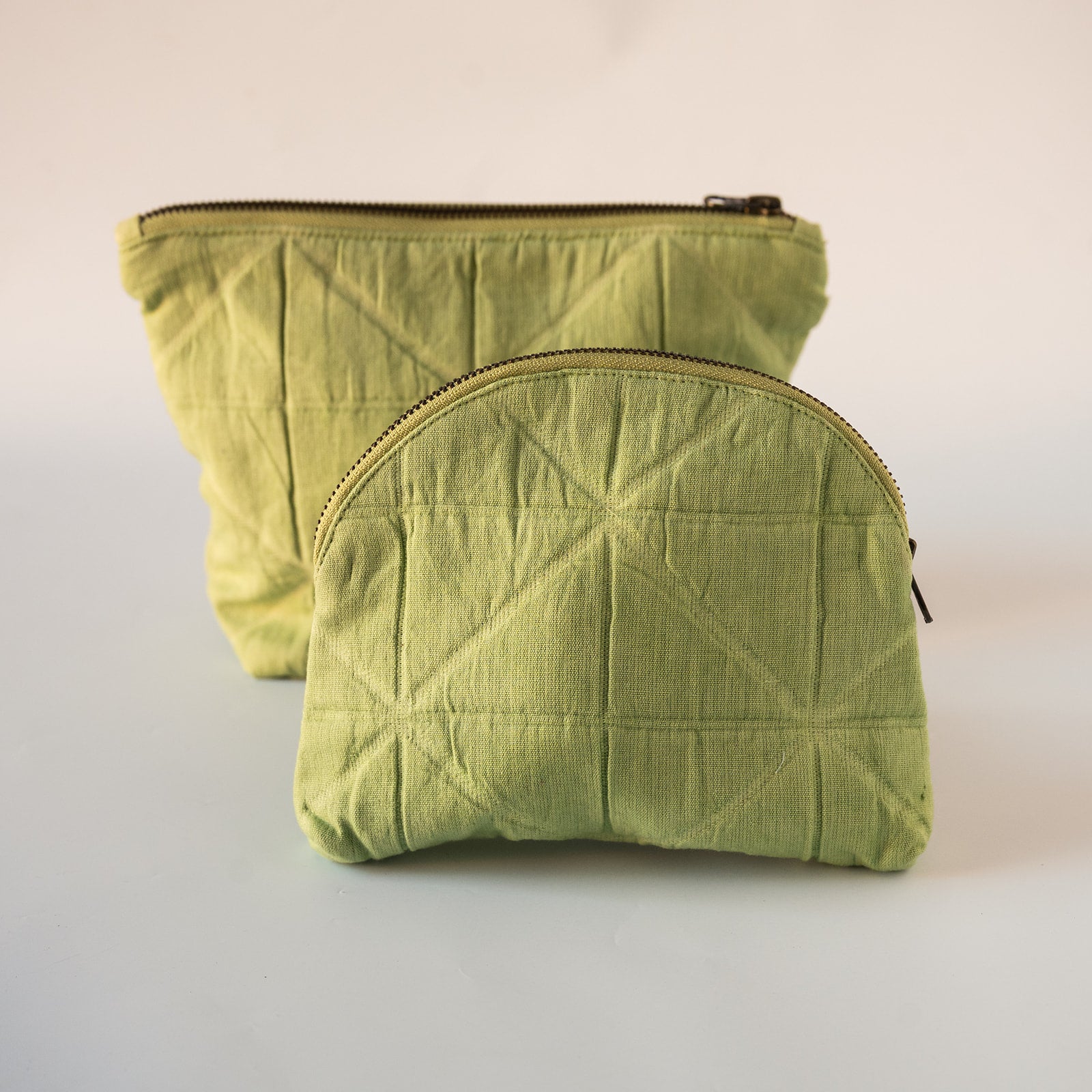 Two quilted fabric zippered pouches in a light olive green color, displayed on a clean off-white background.