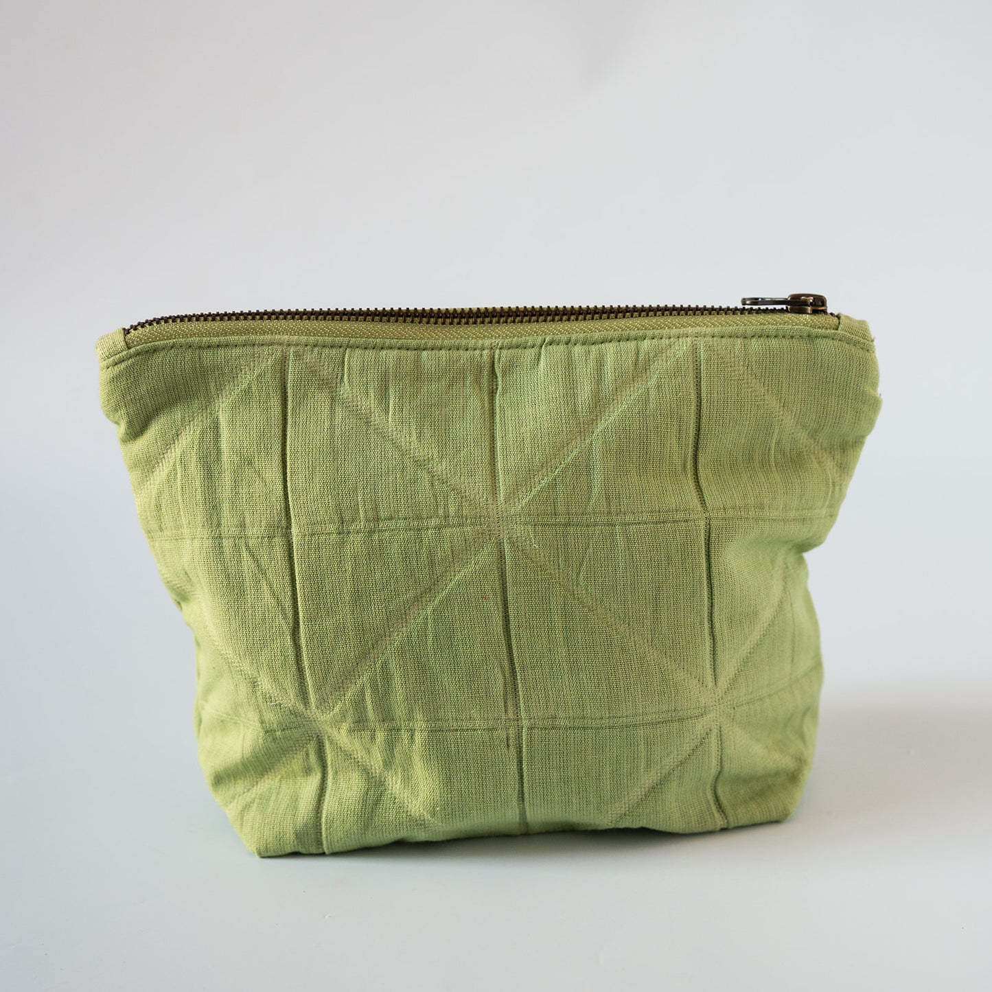 A light olive green quilted fabric pouch with a diagonal stitched geometric pattern and a dark metal zipper, shown on a plain light gray background.