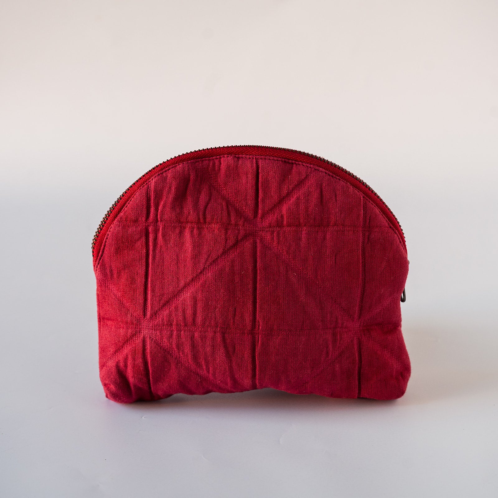 A red quilted cosmetic pouch with a zippered closure, photographed against a plain light background.