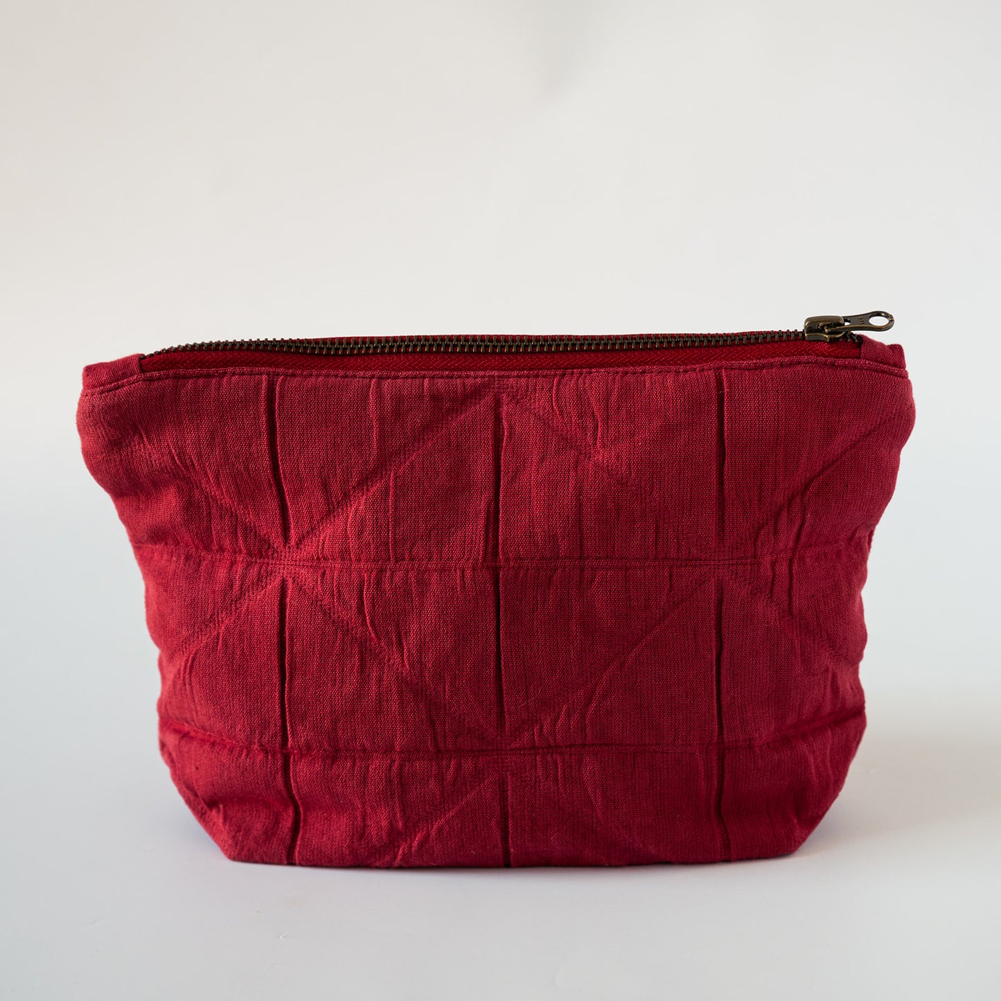 A deep red quilted fabric pouch with a top zipper closure, photographed against a plain white background.