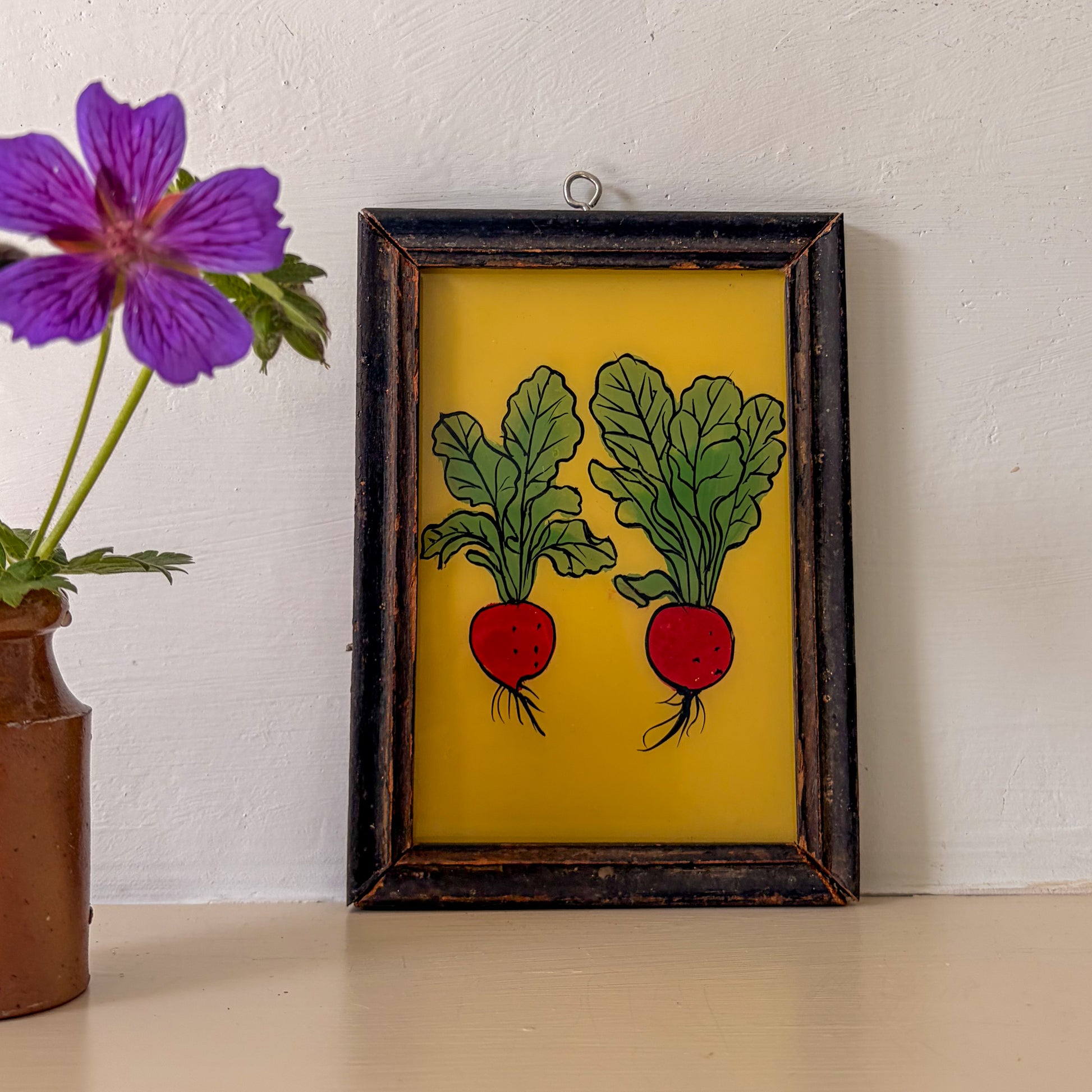 Framed artwork of two radishes on a yellow background with a purple flower in the foreground.