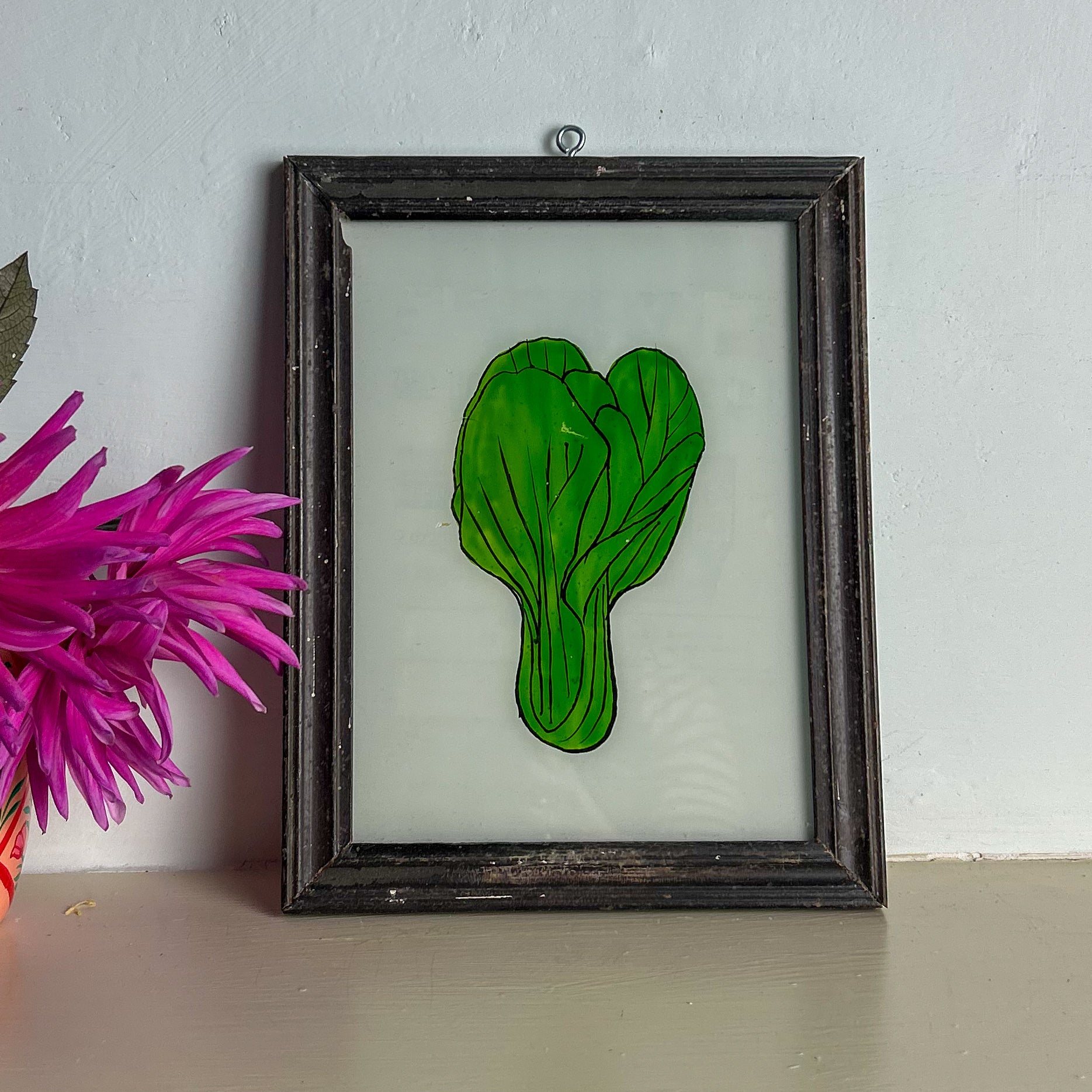 Framed artwork of a green leaf on a white background with a pink flower in the corner.