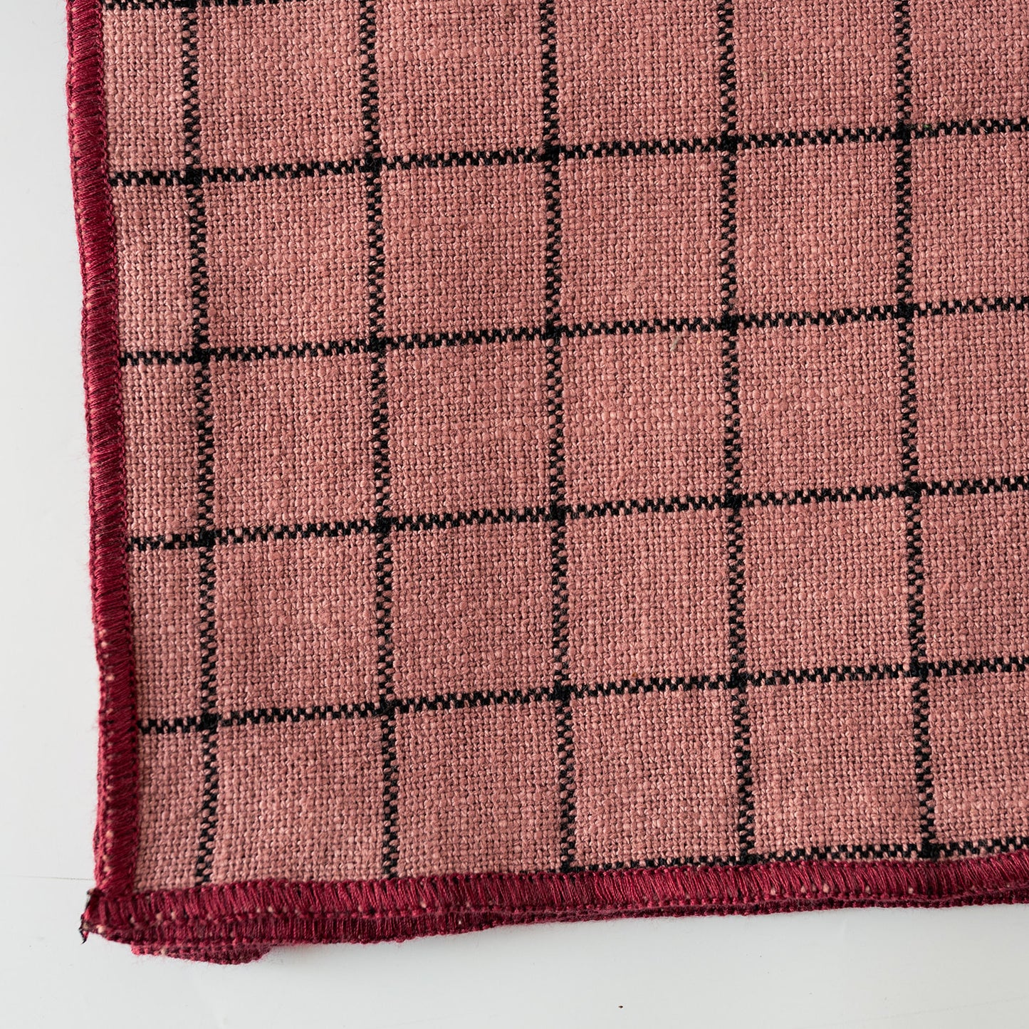 A close-up of a PINK woven textile with a black grid pattern and black stitched border, shown on a white background.