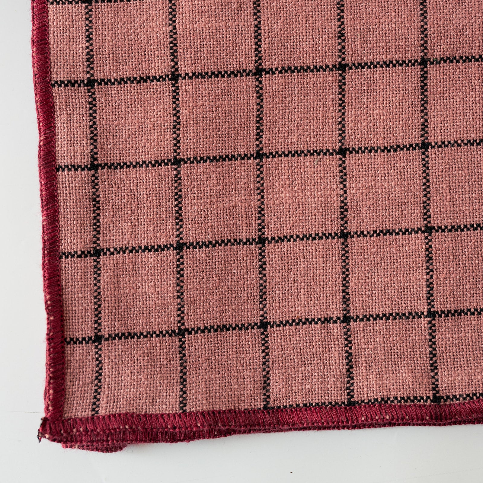 A close-up of a PINK woven textile with a black grid pattern and black stitched border, shown on a white background.