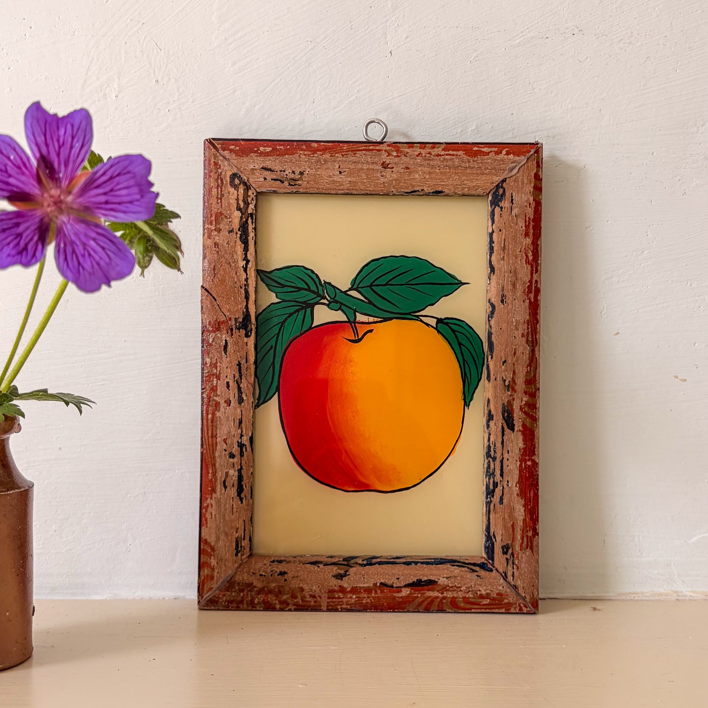 Framed artwork of a peach with a purple flower in the background