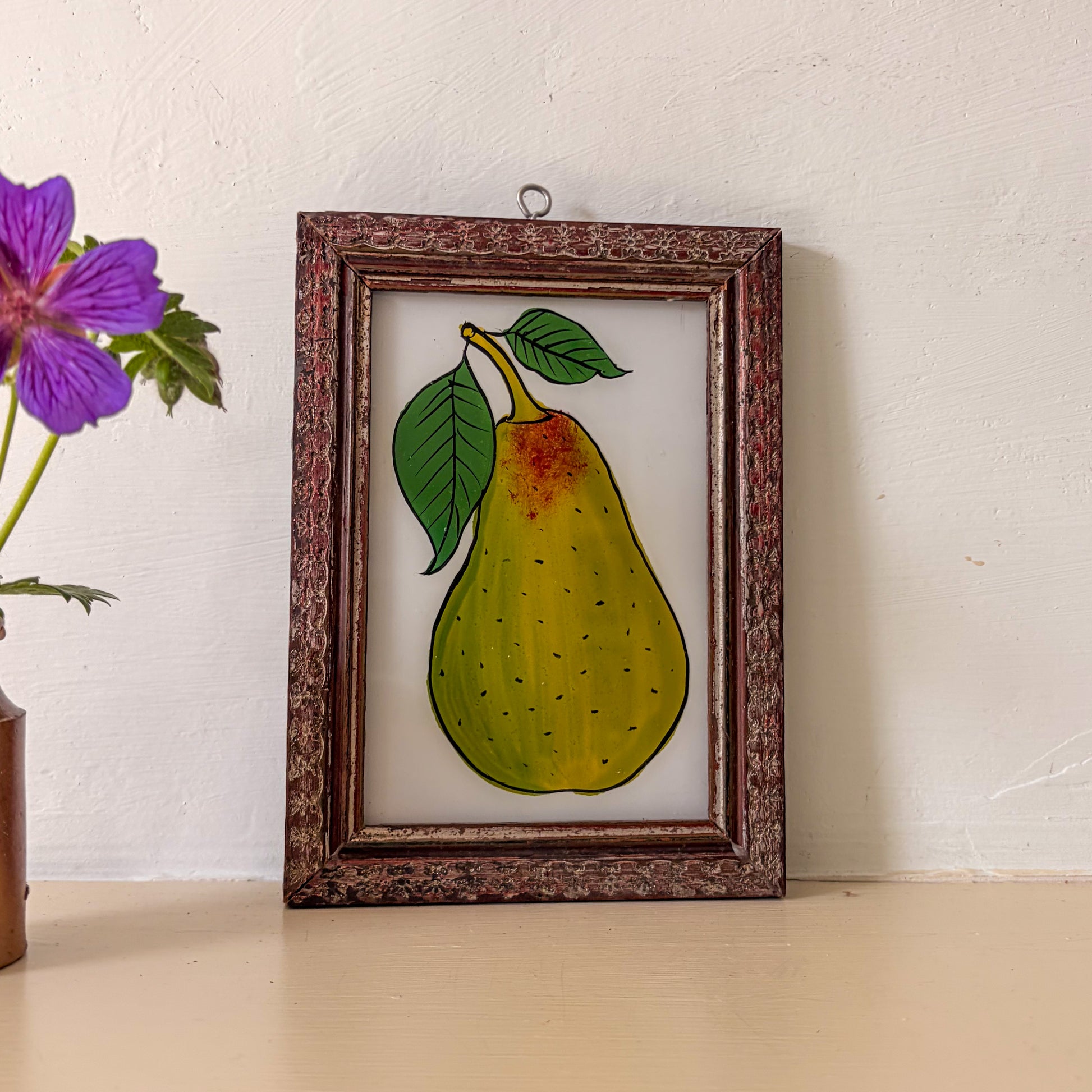 Framed artwork of a pear with leaves on a white wall