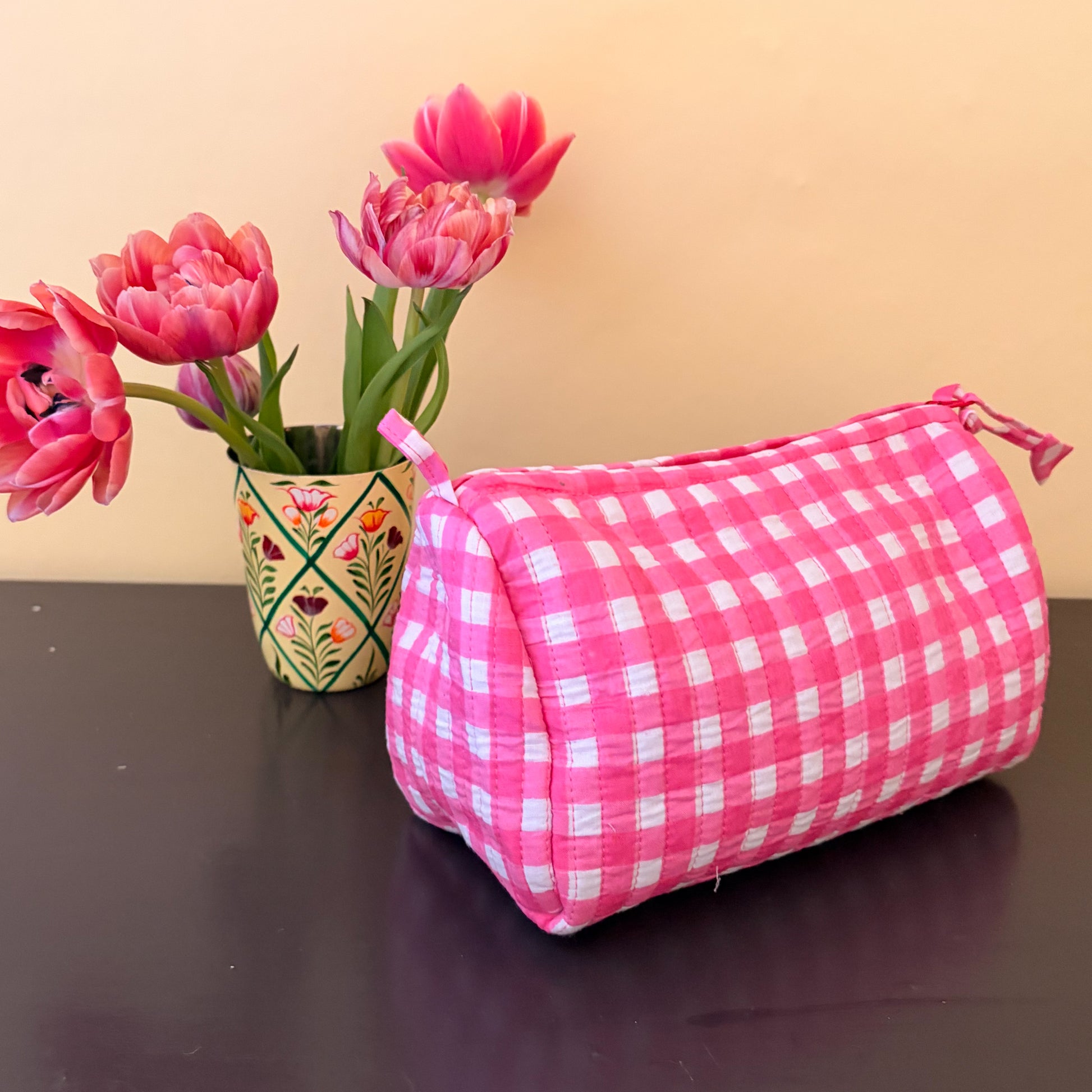 Pink checkered pouch with pink tulips in a pot on a dark surface