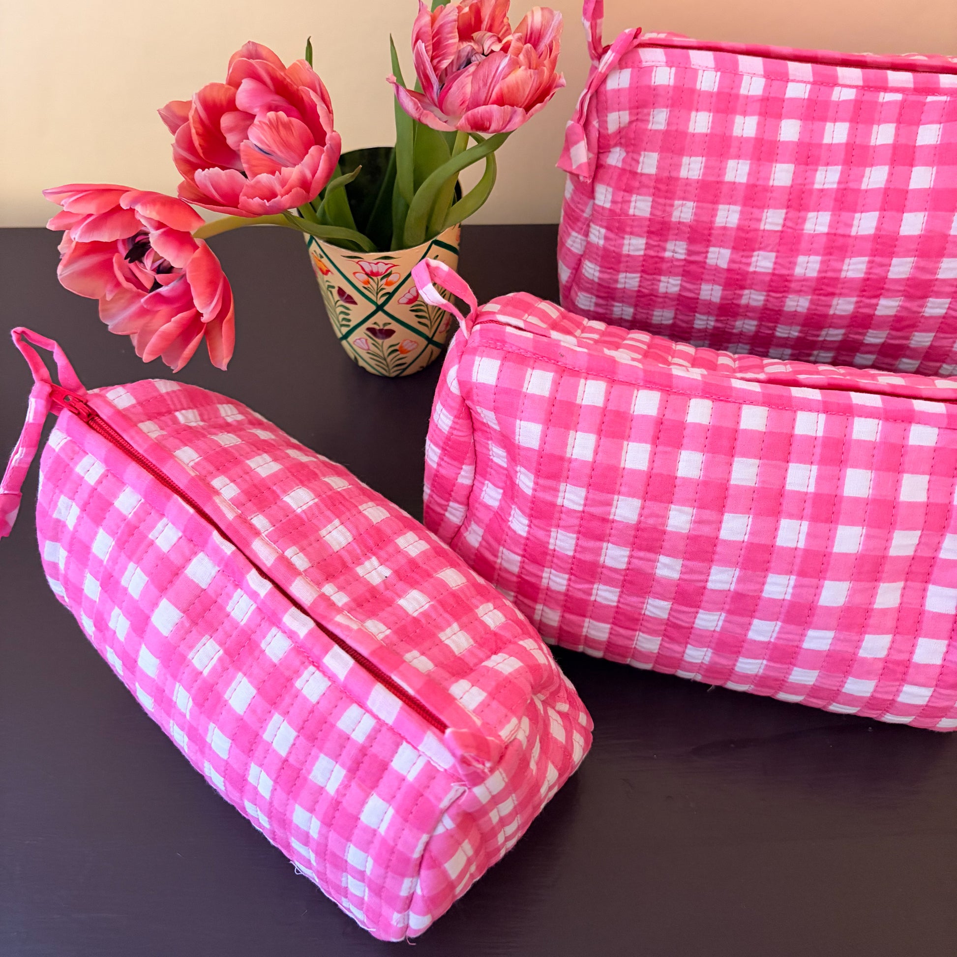 Pink checkered bags on a dark surface with pink tulips in the background