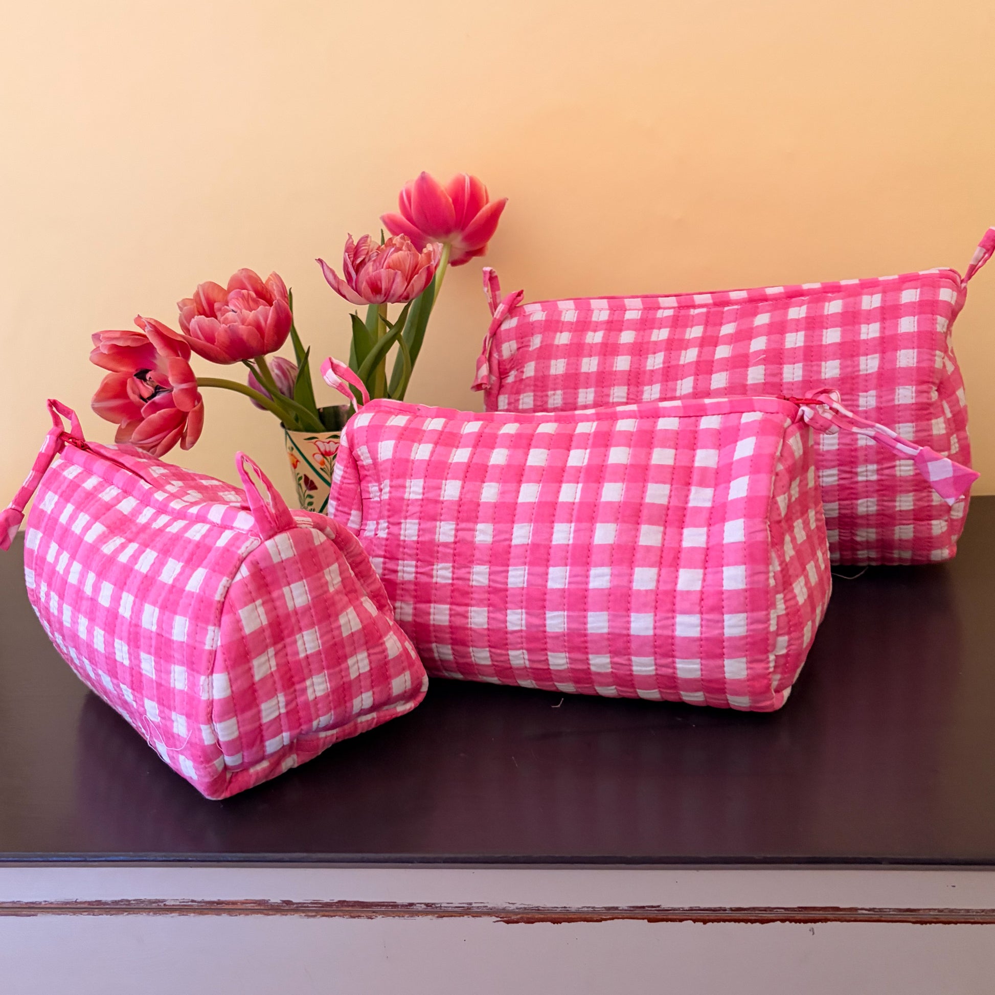Pink checkered cushions on a wooden surface with pink flowers in the background