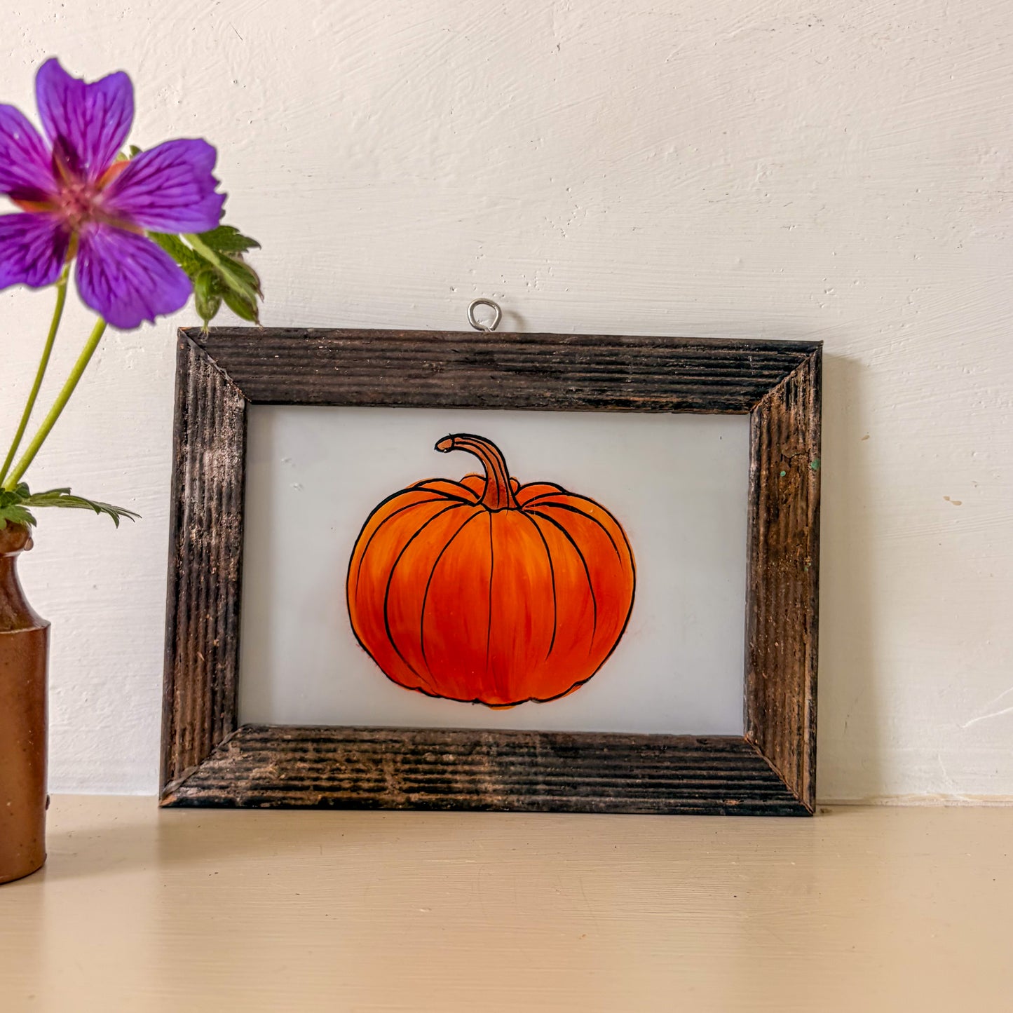 Framed picture of a pumpkin on a table with a purple flower in the background