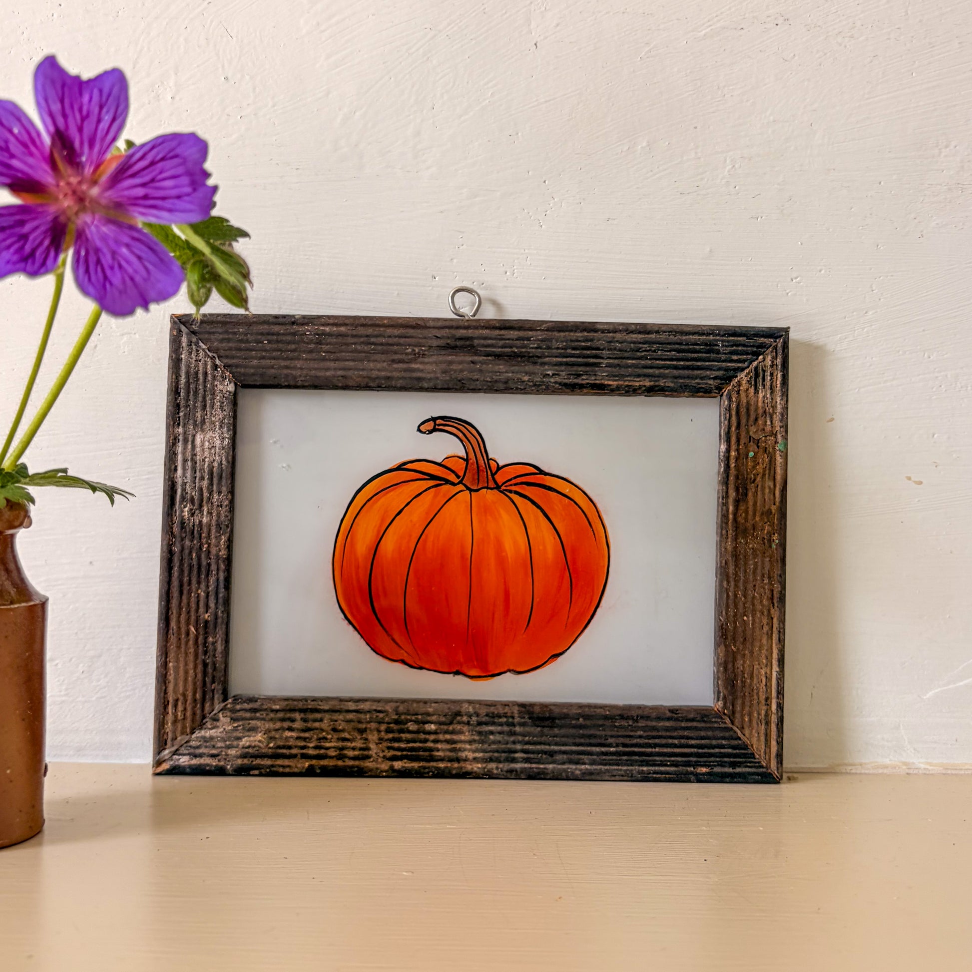 Framed picture of a pumpkin on a table with a purple flower in the background