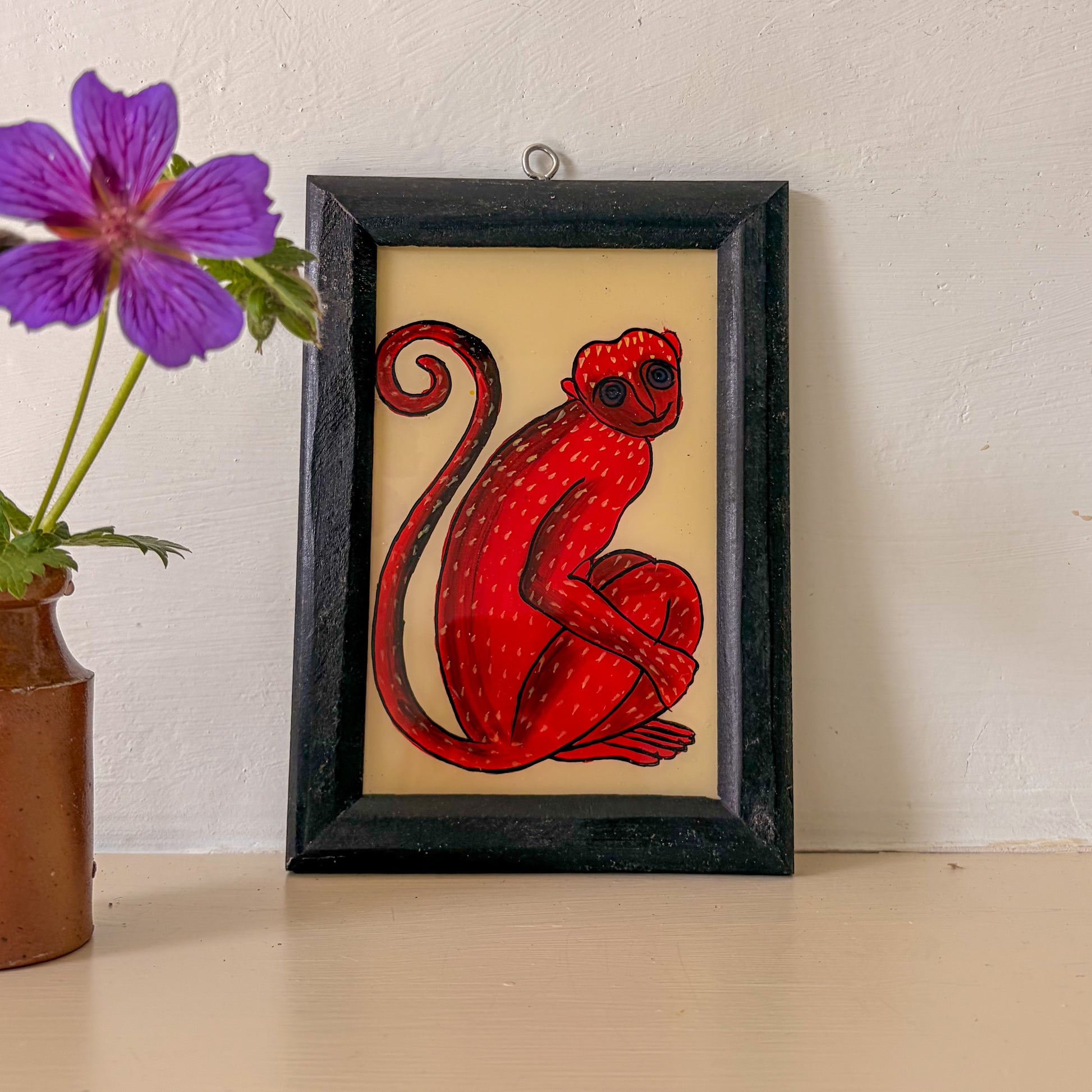 Framed artwork of a red monkey on a beige background with a purple flower in the corner.