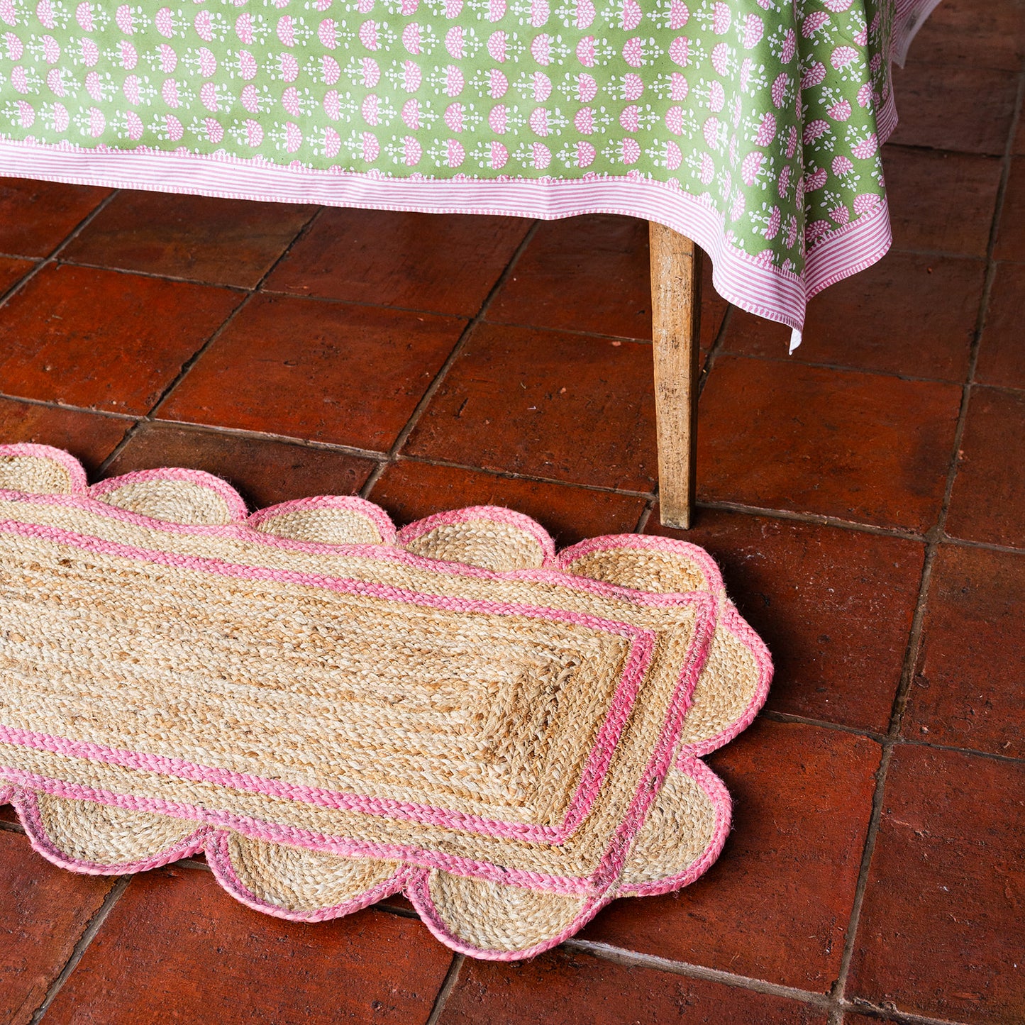 Scallop-edged doormat with pink trim on a terracotta tiled floor.