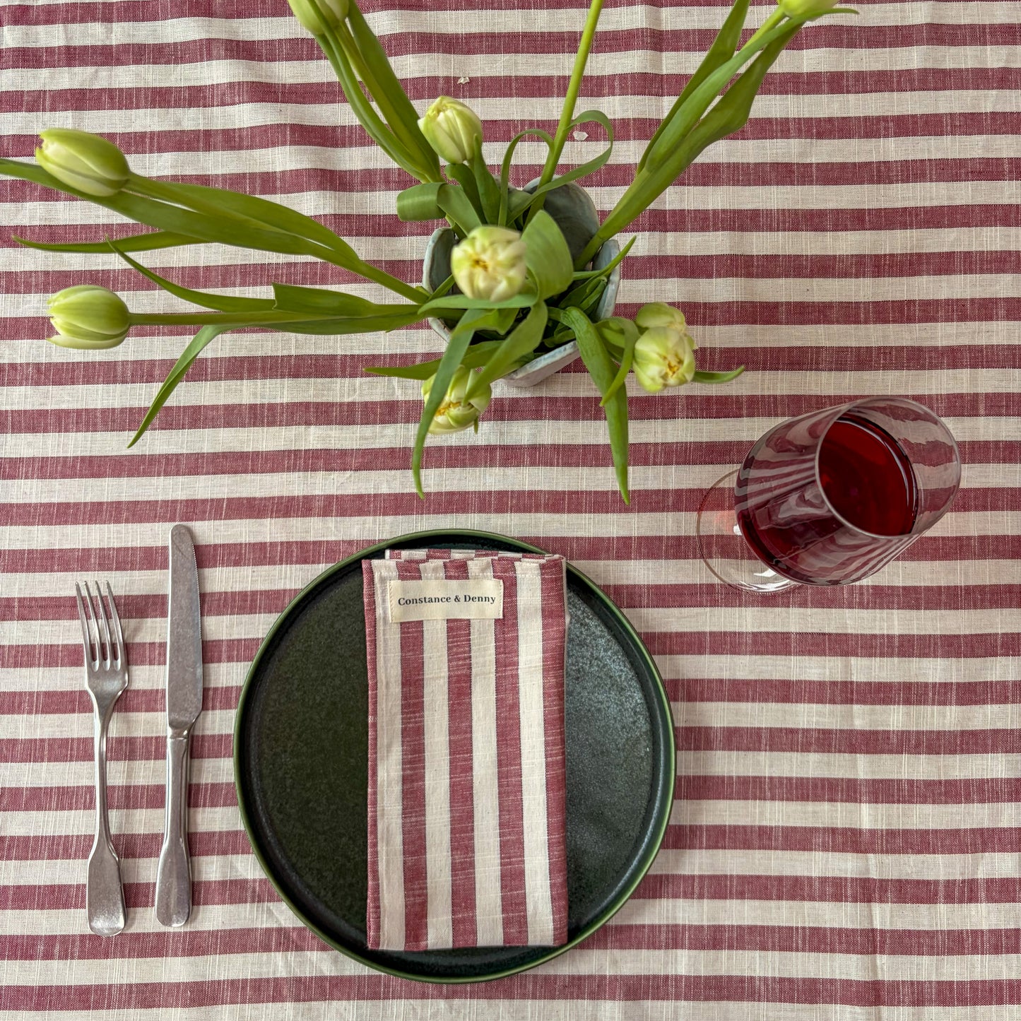 Dining table setting with striped tablecloth, black plate, silverware, and floral arrangement.
