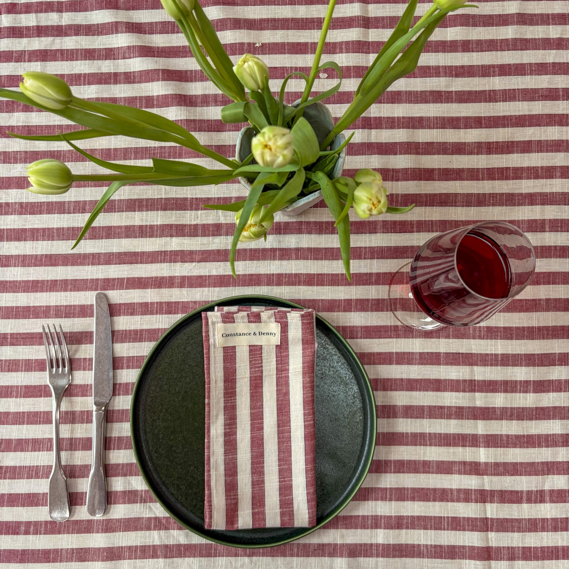 Dining table setting with striped tablecloth, black plate, silverware, and floral arrangement.