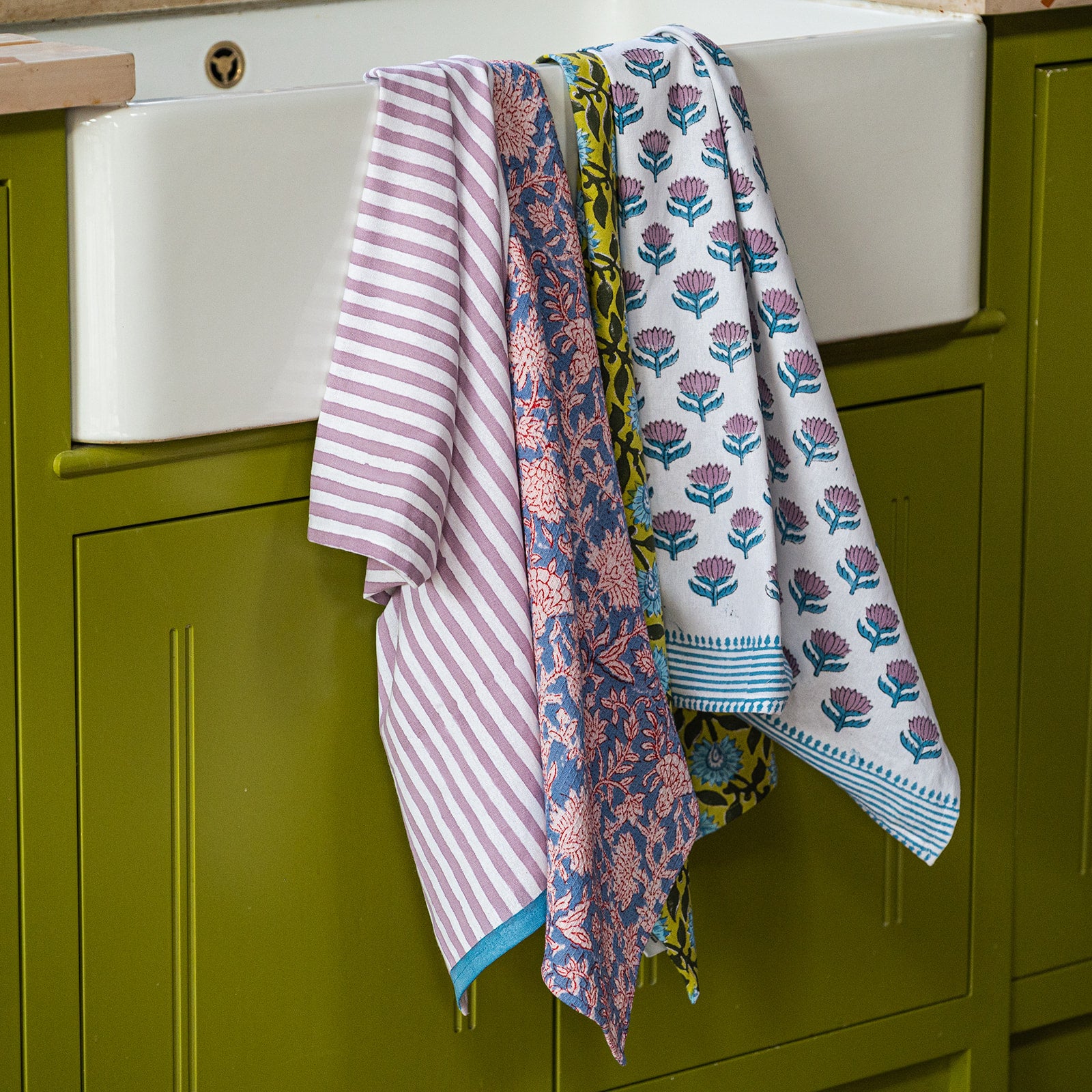 Patterned towels hanging on a kitchen sink with green cabinets in the background