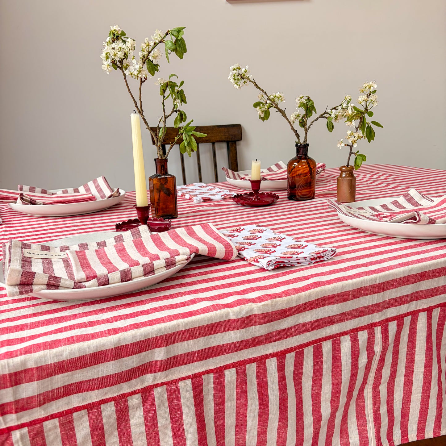 Dining table set with red and white striped tablecloth, plates, napkins, and decorative vases.