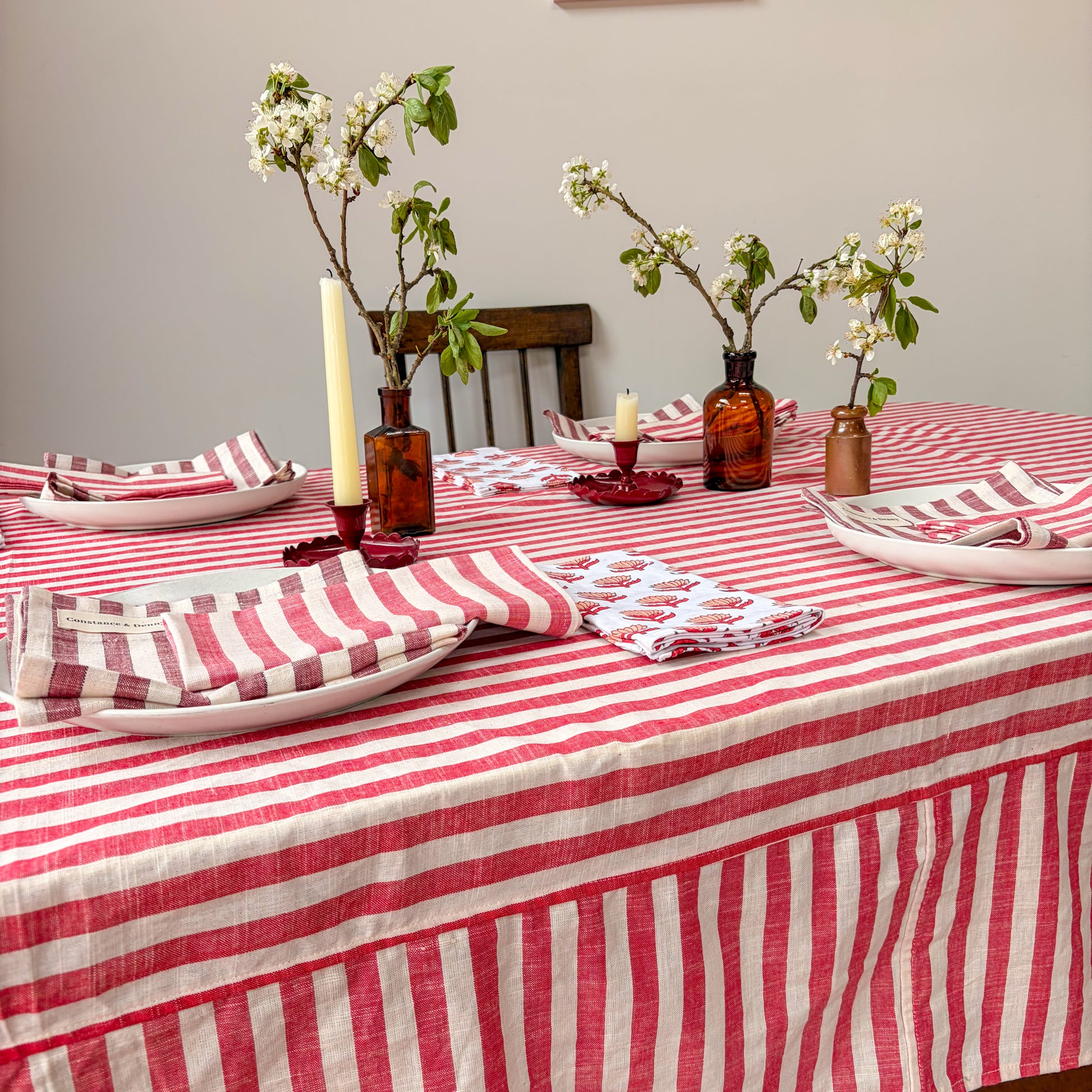 Dining table set with red and white striped tablecloth, plates, napkins, and decorative vases.
