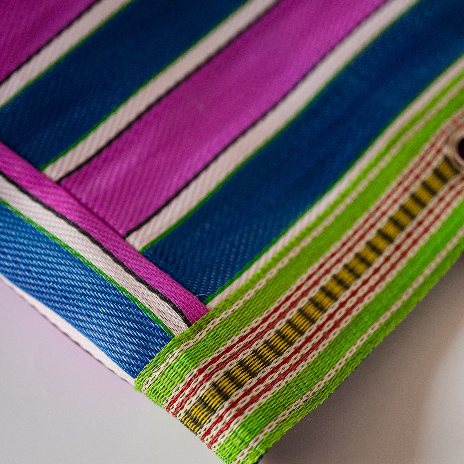 Close-up of a striped woven textile corner with bold magenta, blue, white, green, red, and yellow bands.