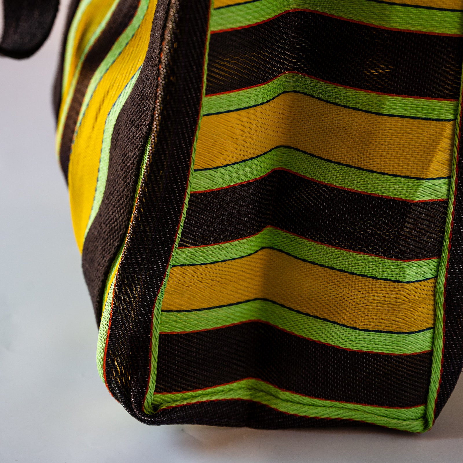 Close-up of a woven fabric bag or tote with bold horizontal stripes in yellow, lime green, and black, showing the texture and construction details.