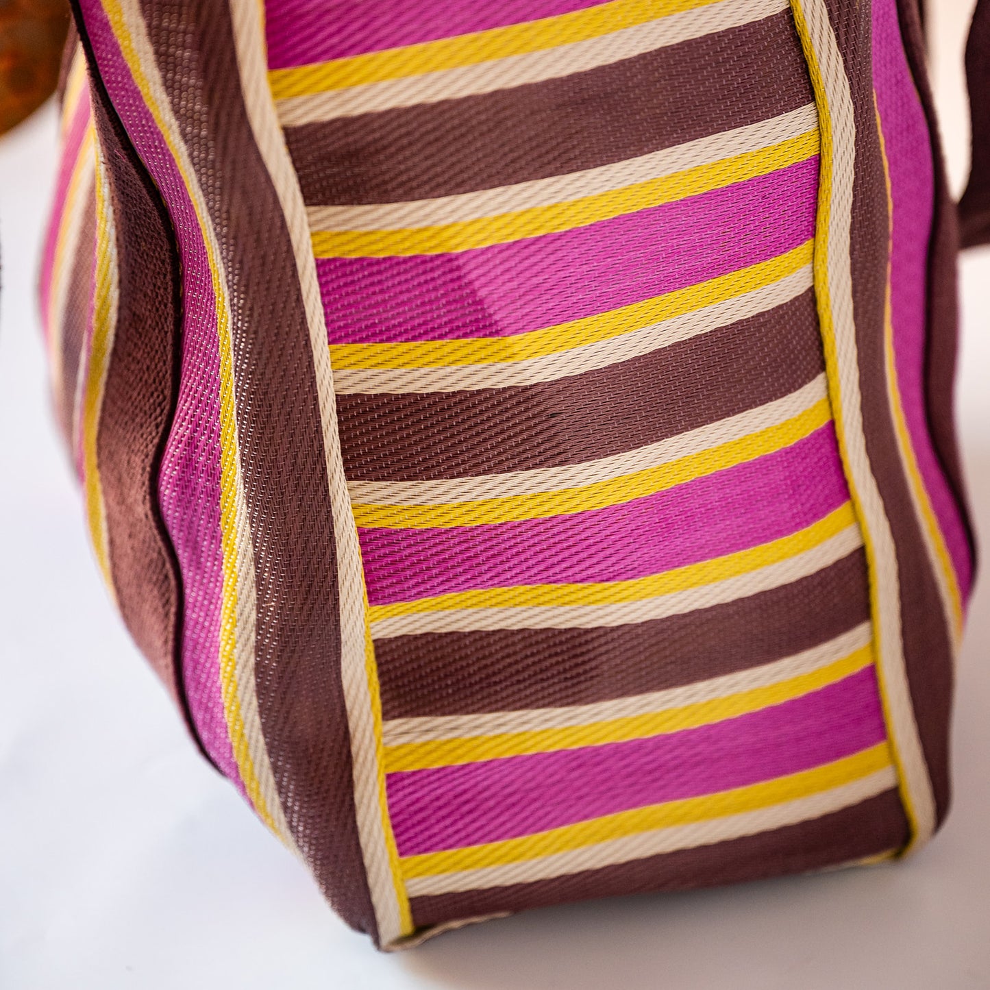 A close-up of a woven tote bag with horizontal stripes in brown, magenta pink, yellow, and off-white.