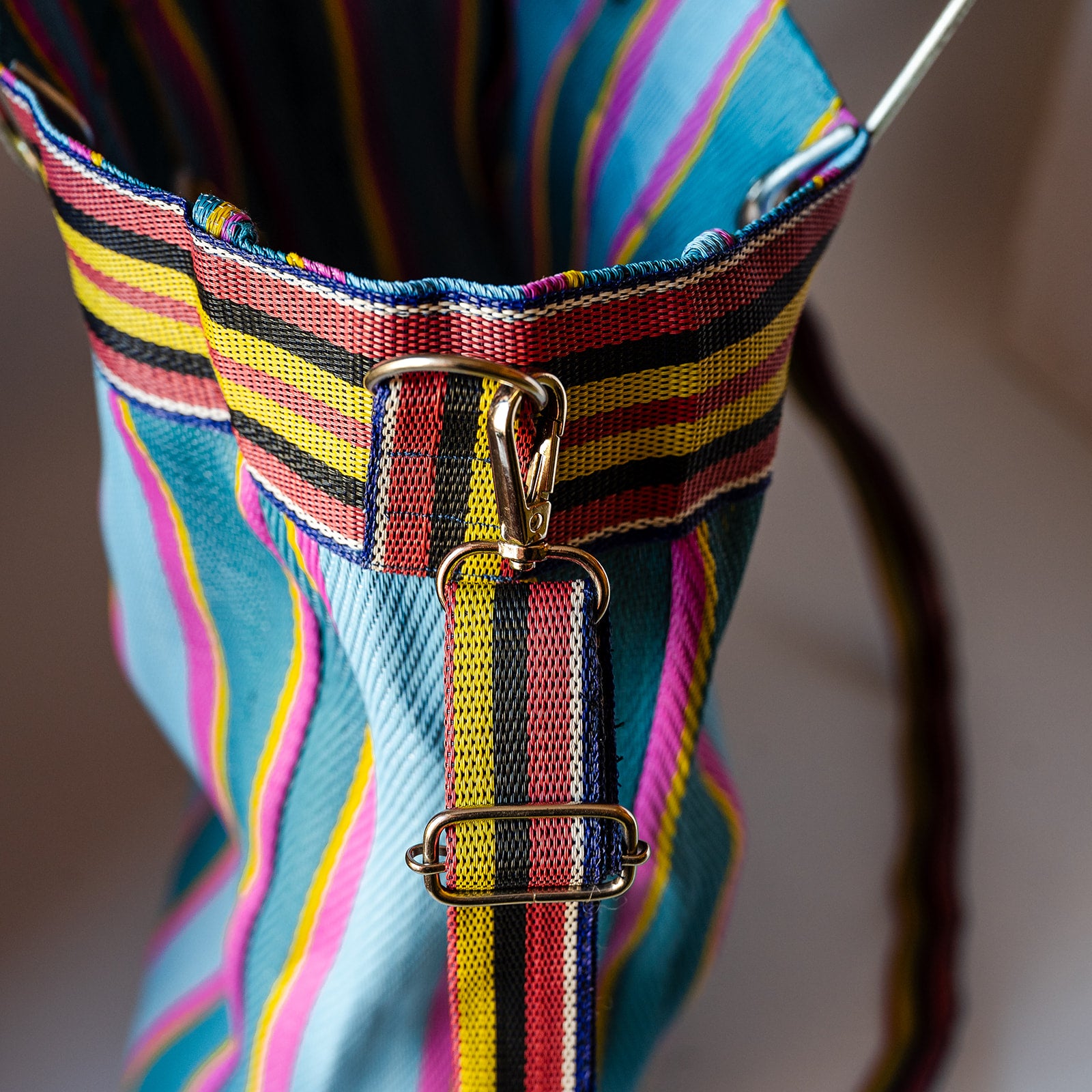 Close-up of a colorful striped fabric bag with blue, pink, yellow, and black vertical stripes, featuring a metal clasp and strap attachment.