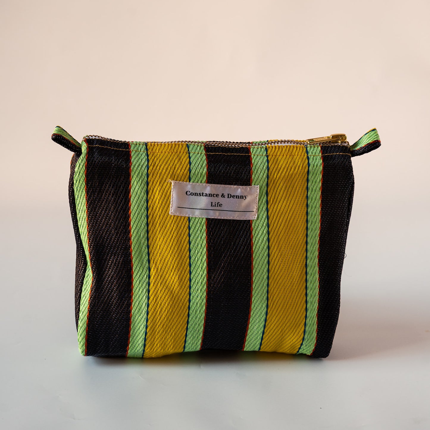 A small zippered cosmetic pouch with vertical stripes in black, yellow, and light green, featuring a white label that reads 'Constantine & Dennis life'.
