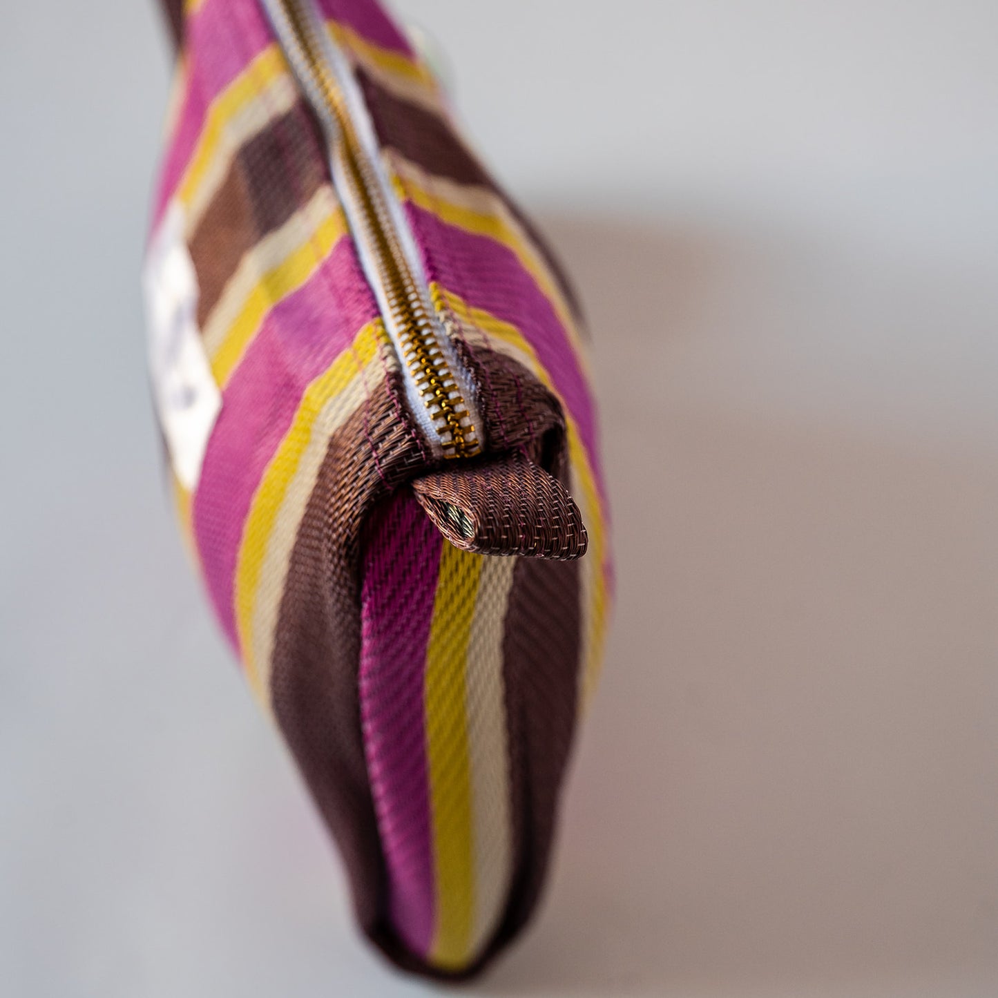 Close-up of a striped fabric pouch with a gold zipper, featuring pink, brown, yellow, and white plaid pattern.