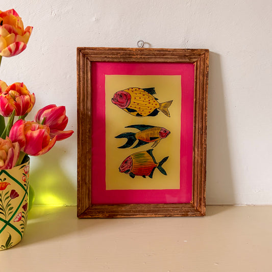Framed artwork of fish on a pink background next to a vase of flowers.