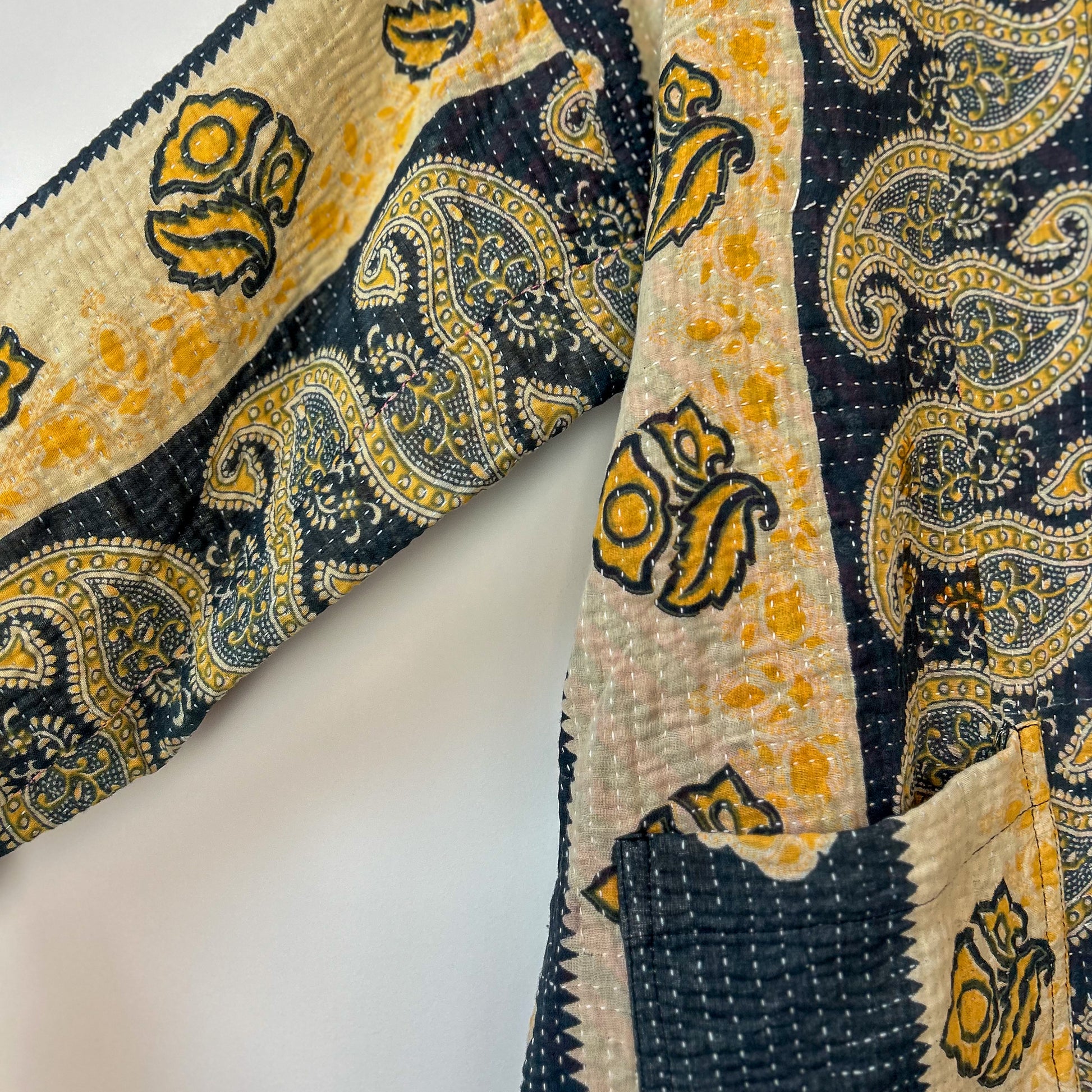 Close-up of a patterned fabric with yellow and black designs on a white background. Vintage-kantha-jacket-handmade-unique-37-paisley-pattern-sleeve