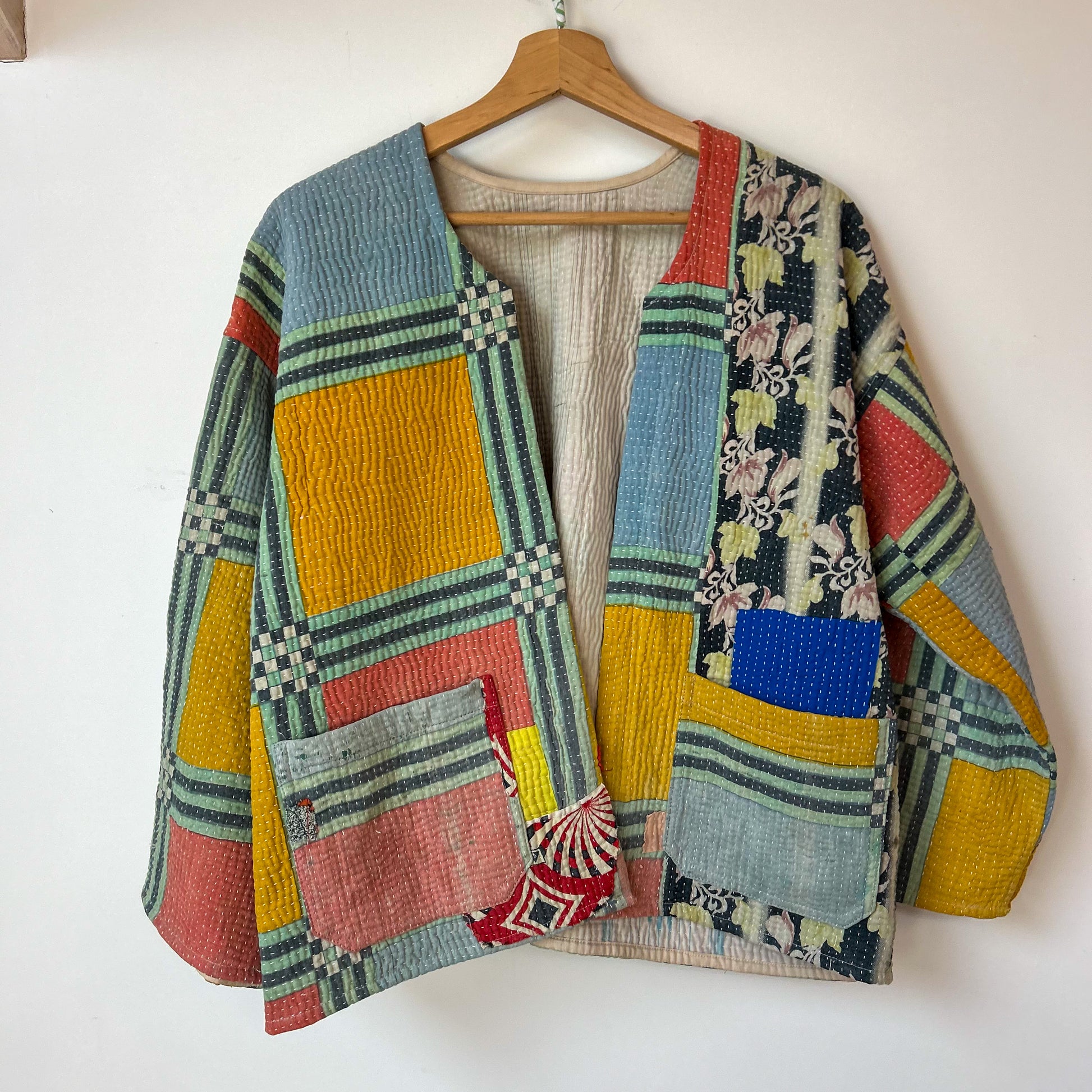Colorful patchwork cardigan on a wooden hanger against a white background. te floral patterns on a white background. Vintage-kantha-jacket-handmade-unique-39-geometric-colourful