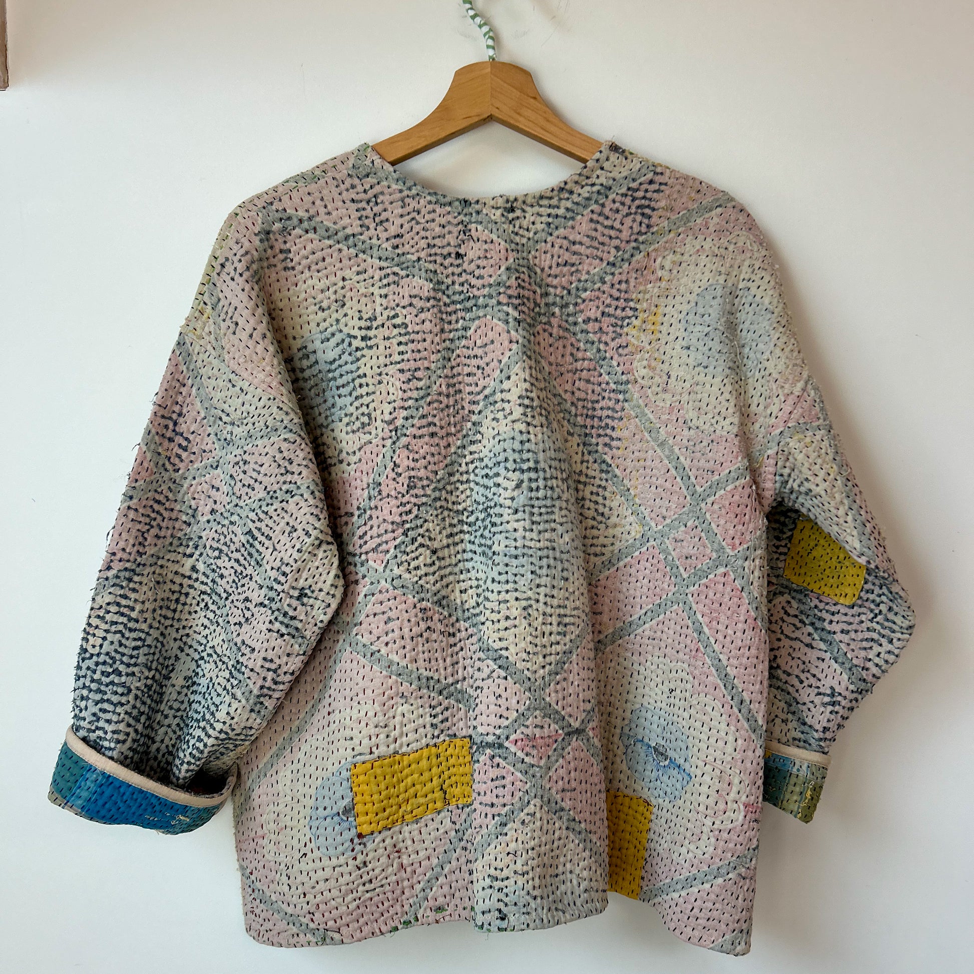 Multicolored textured sweater on a wooden hanger against a white background. Vintage-kantha-jacket-handmade-unique-40-textured-reverse