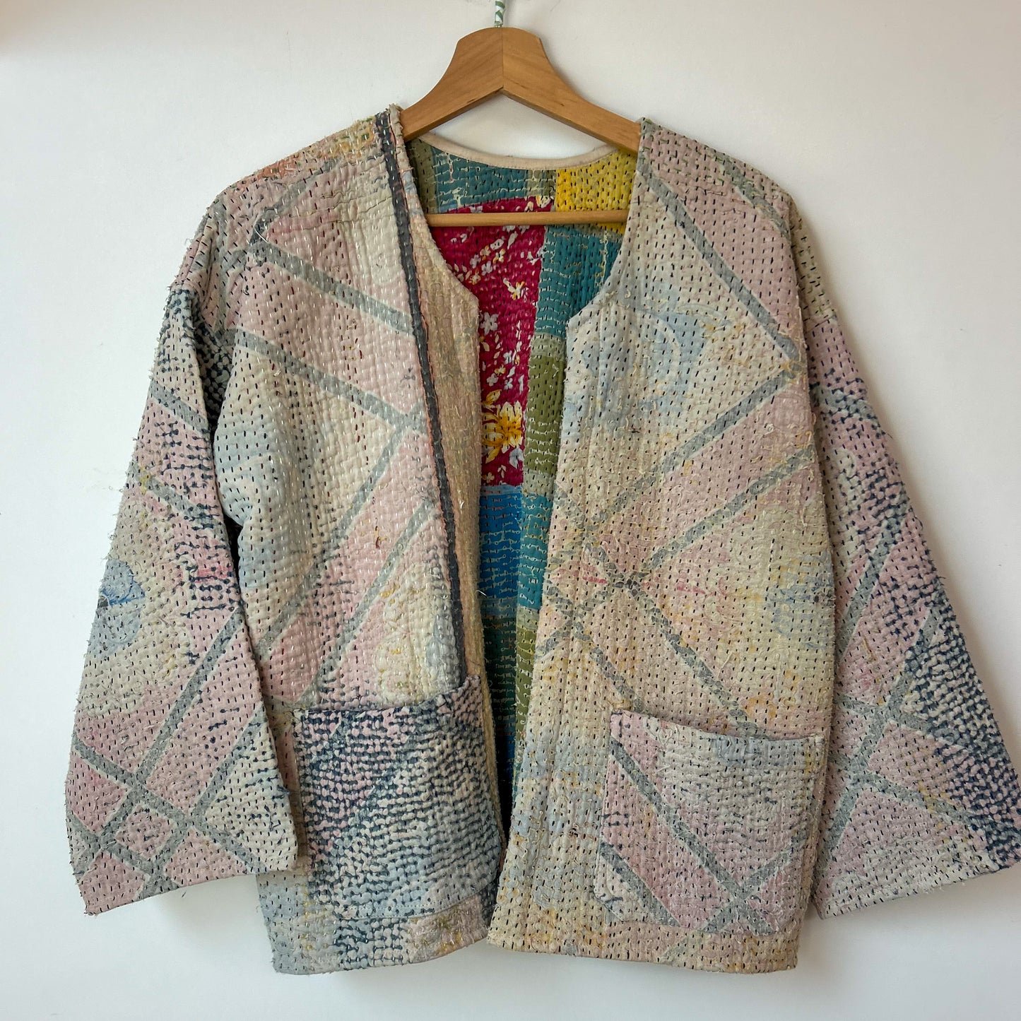 Multicolored textured jacket on a wooden hanger against a white background. Vintage-kantha-jacket-handmade-unique-40-textured