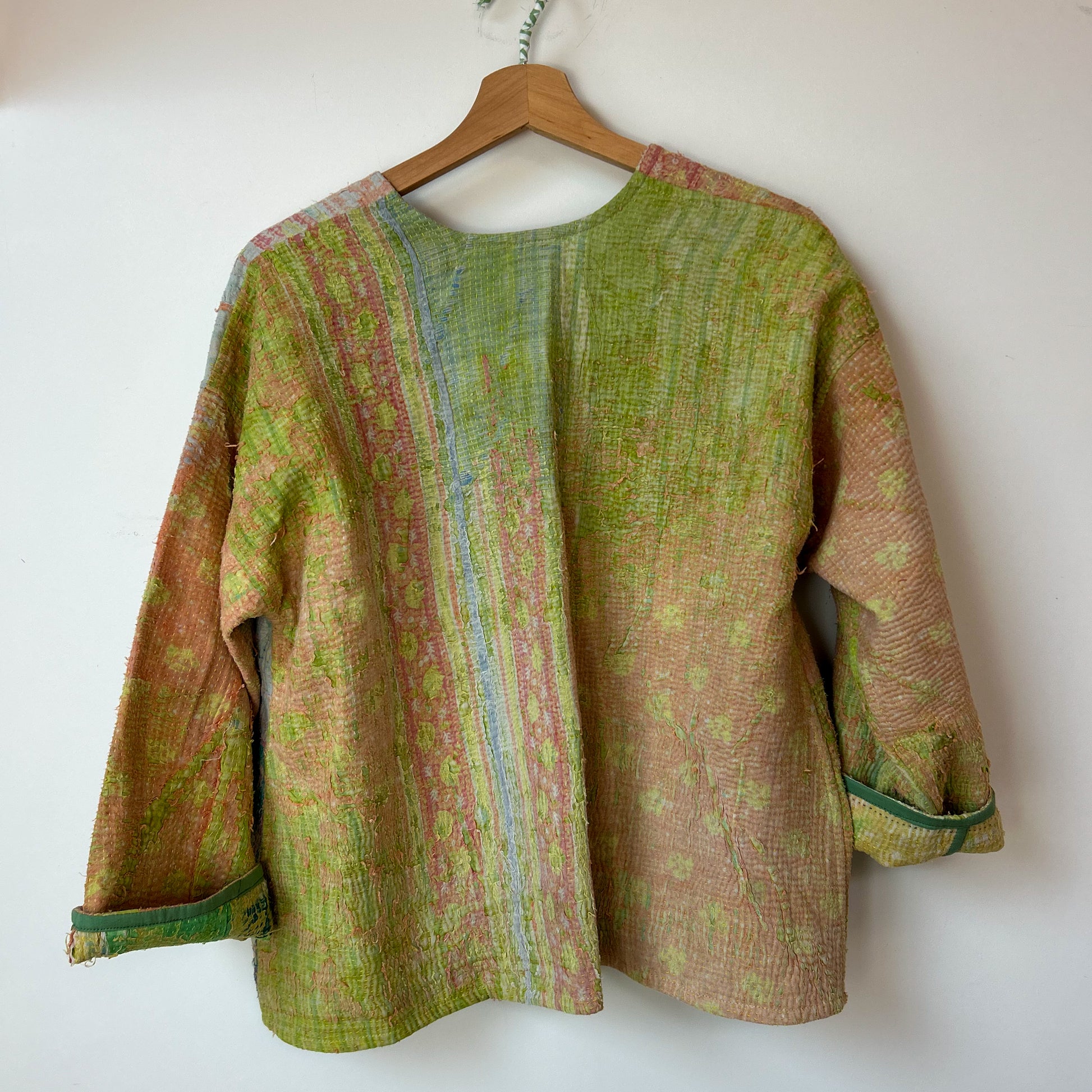 Textured jacket with a mix of green and brown colors on a hanger against a white background. Vintage-kantha-jacket-handmade-unique-41-textured-reverse