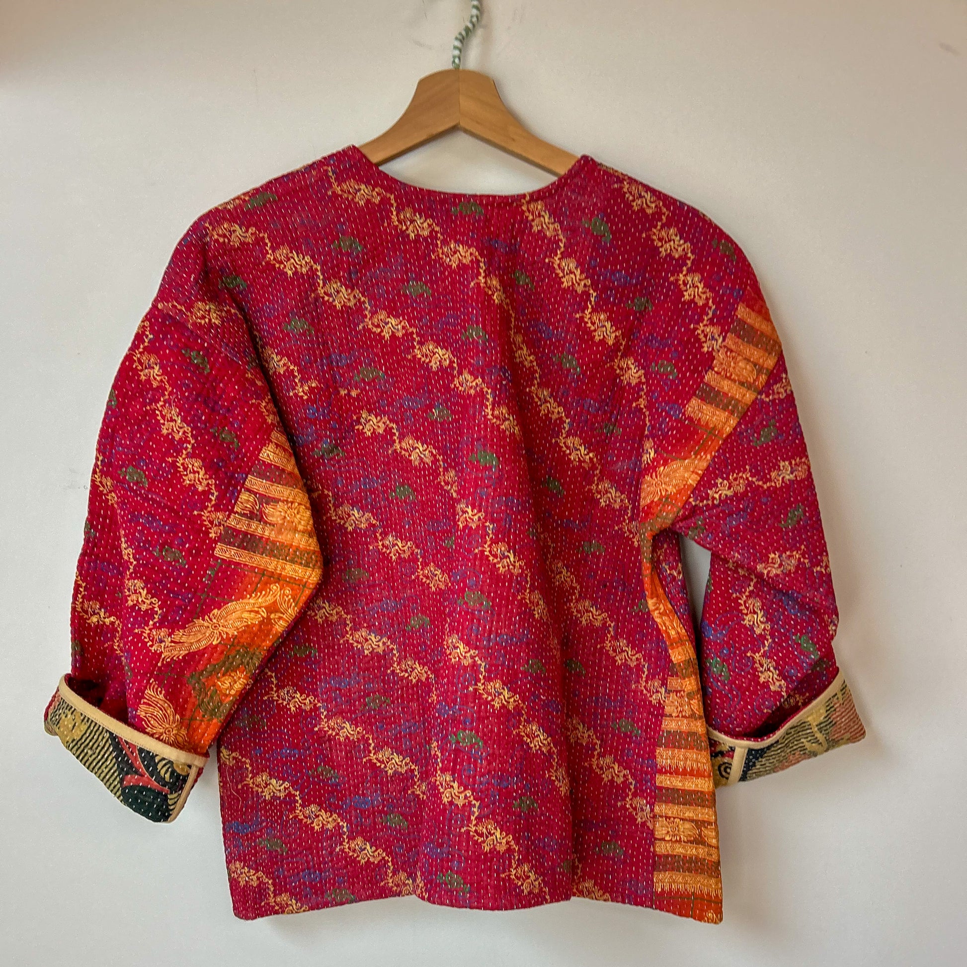 Red patterned jacket on a hanger against a white background. Vintage-kantha-jacket-handmade-unique-43-reverse