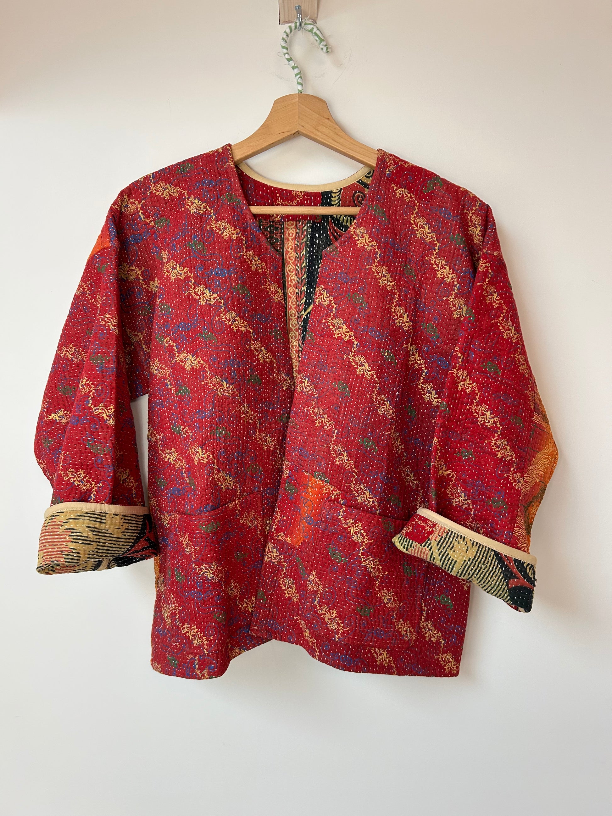 Red patterned jacket on a hanger against a white background. Vintage-kantha-jacket-handmade-unique-43