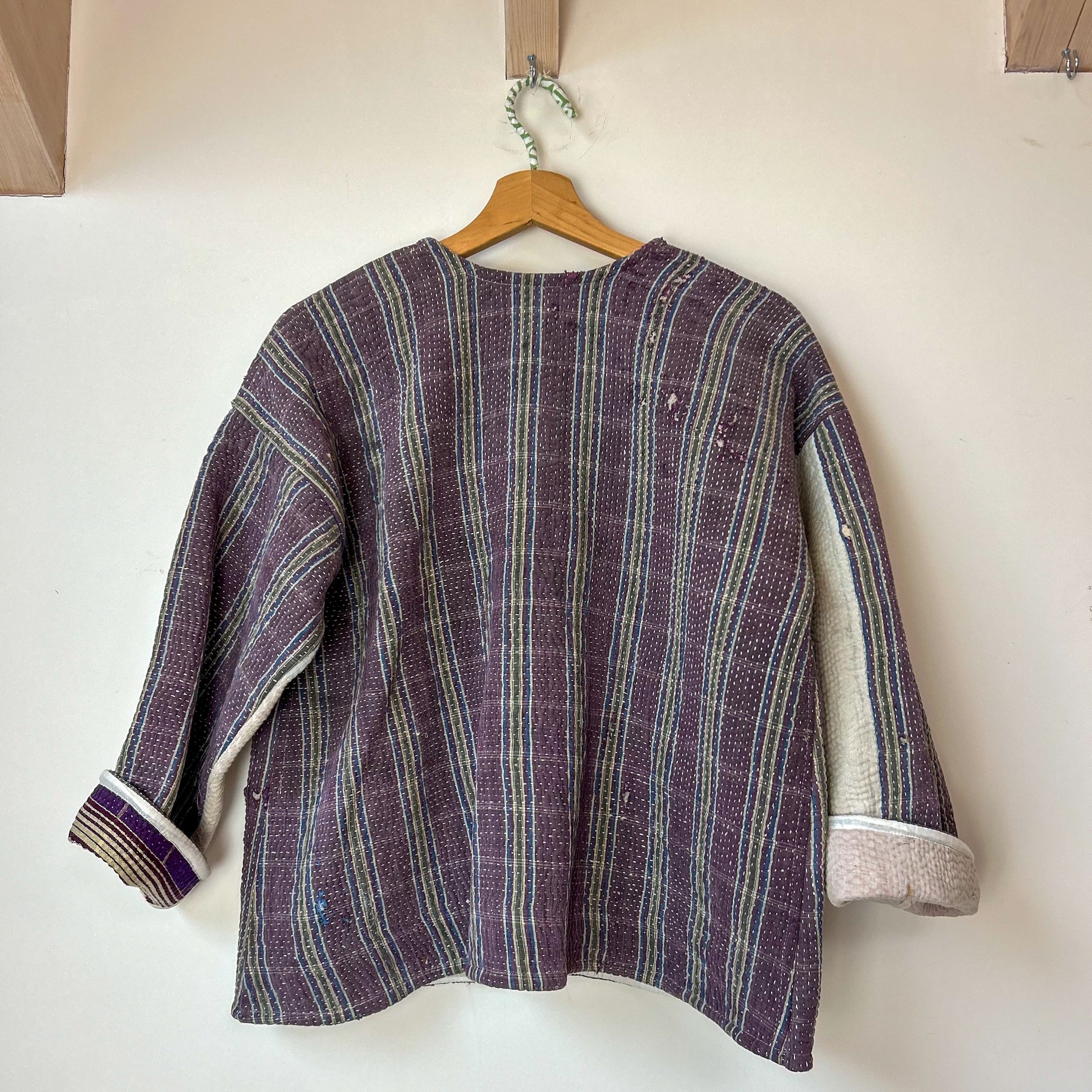 Striped jacket on a wooden hanger against a white wall. Vintage-kantha-jacket-handmade-unique-mauve-34-reverse