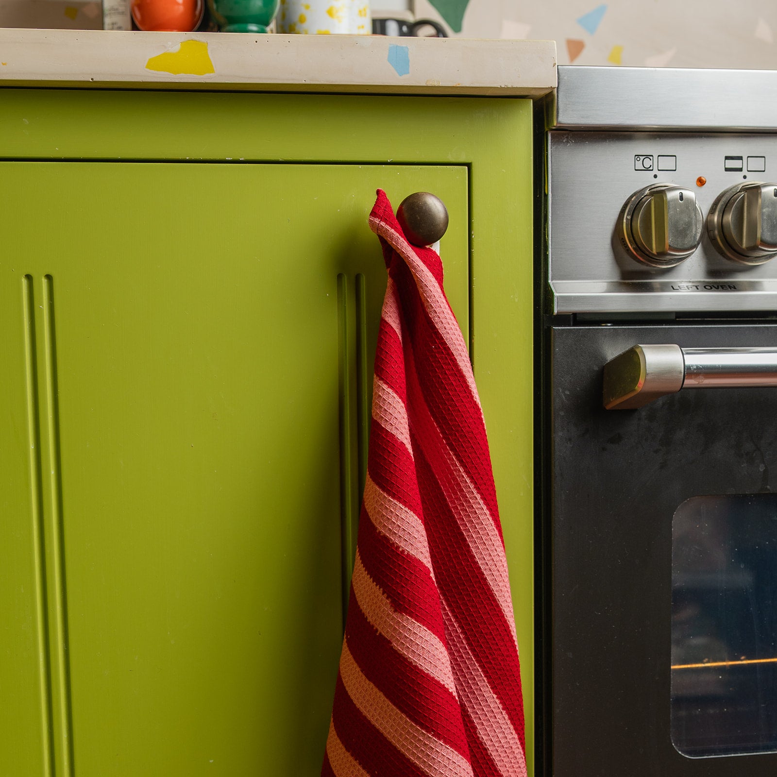 Red and white striped towel hanging on a green cabinet next to a silver oven.