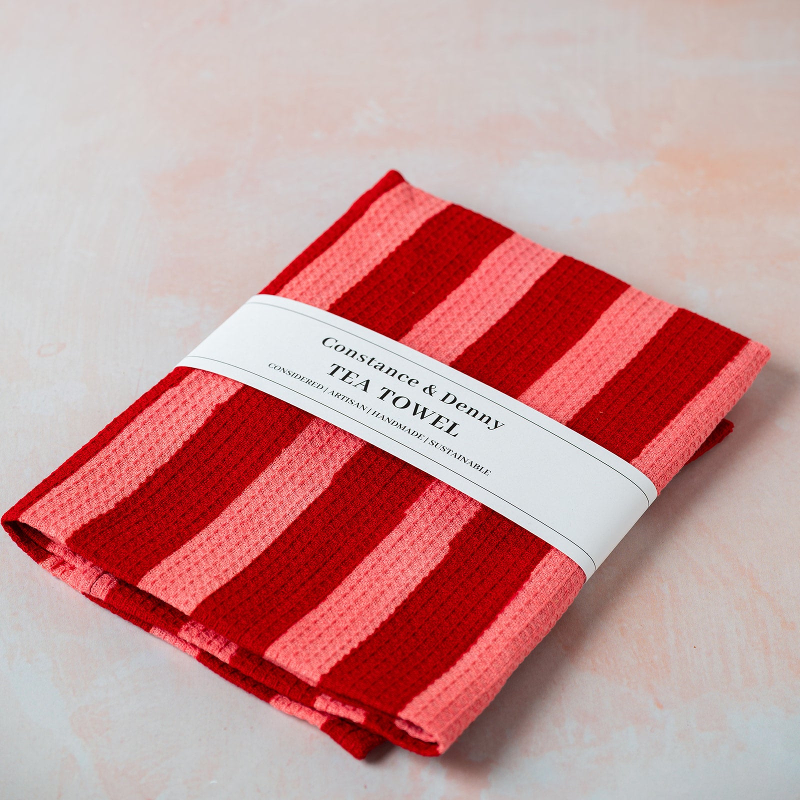 Red striped tea towel with a white label on a light pink background