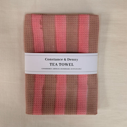 Waffle-textured tea towel with pink and brown stripes on a beige background, branded 'Constance & Denny'.