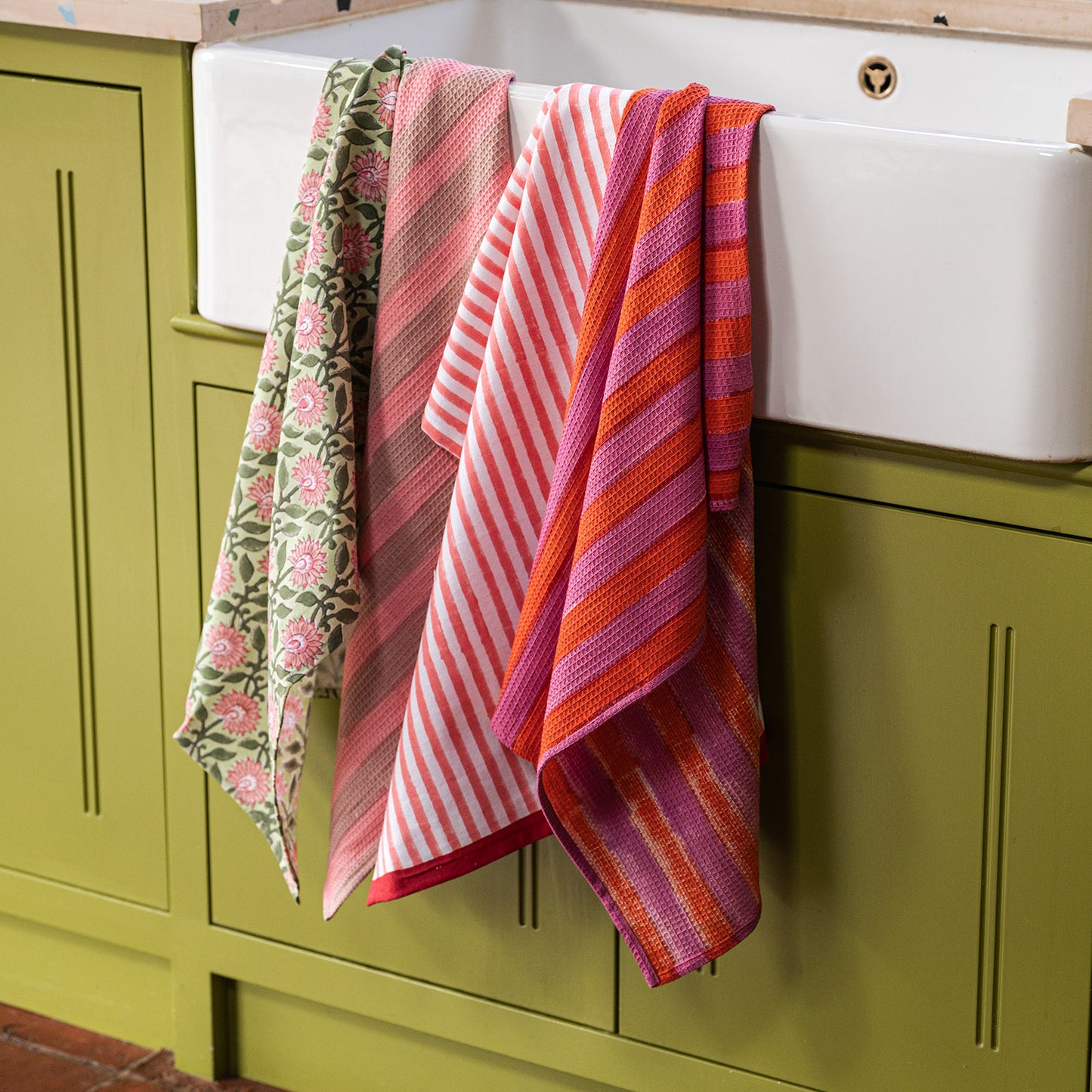 Colorful kitchen towels hanging on a white cabinet with green cabinets in the background