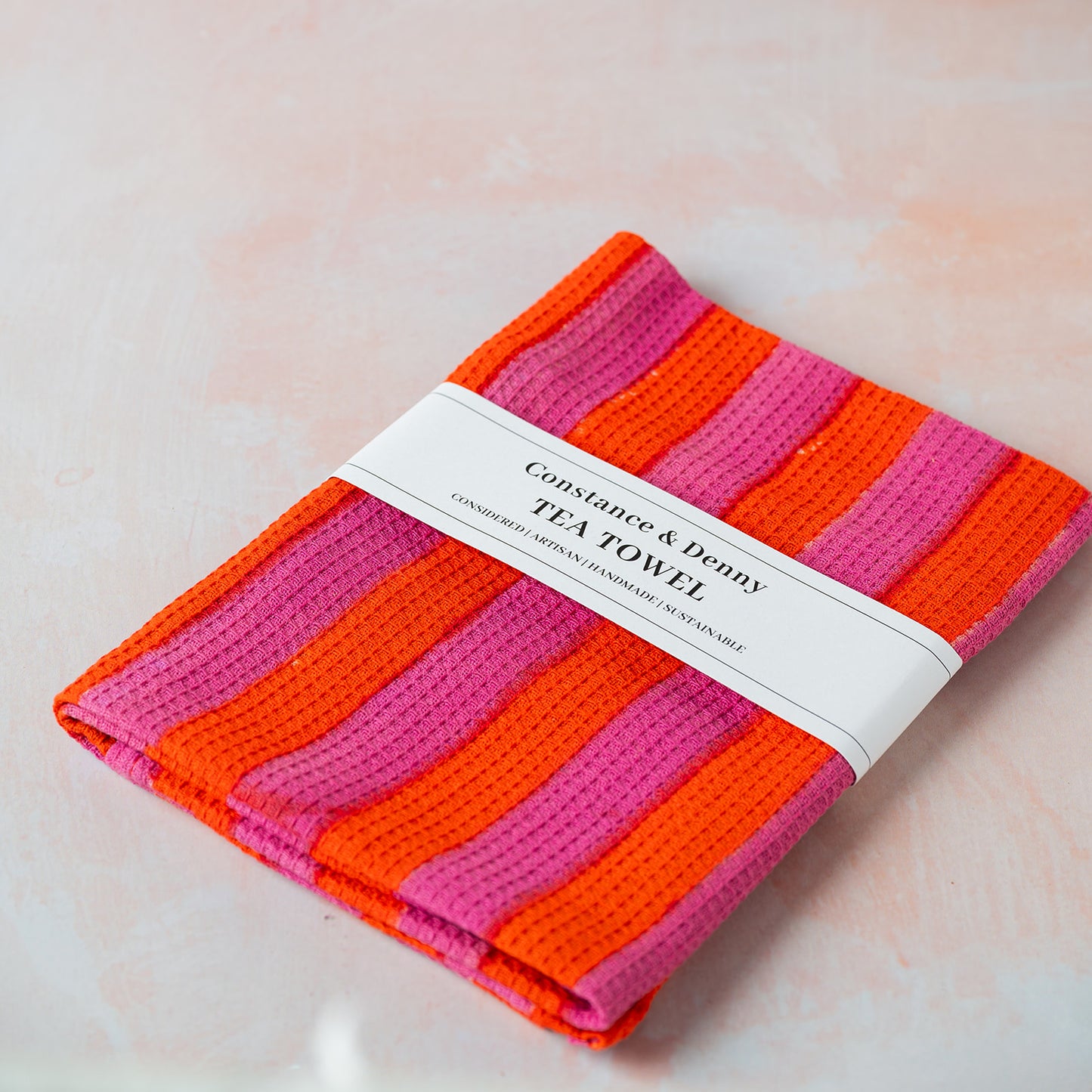 Pink and orange striped tea towel with a label on a light background