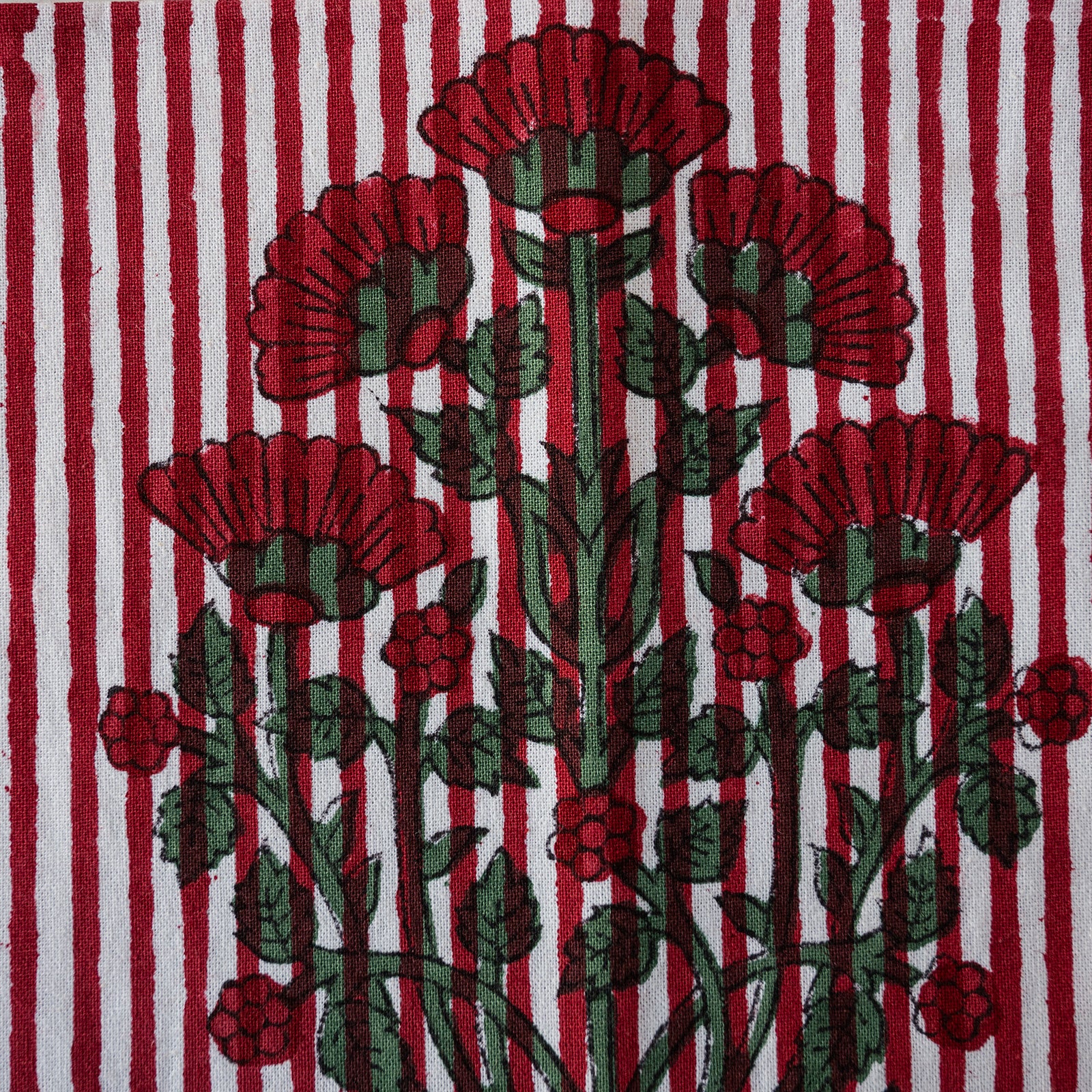 A close-up of a woven textile featuring a stylized floral pattern with red flowers and green leaves over a red-and-white striped background.
