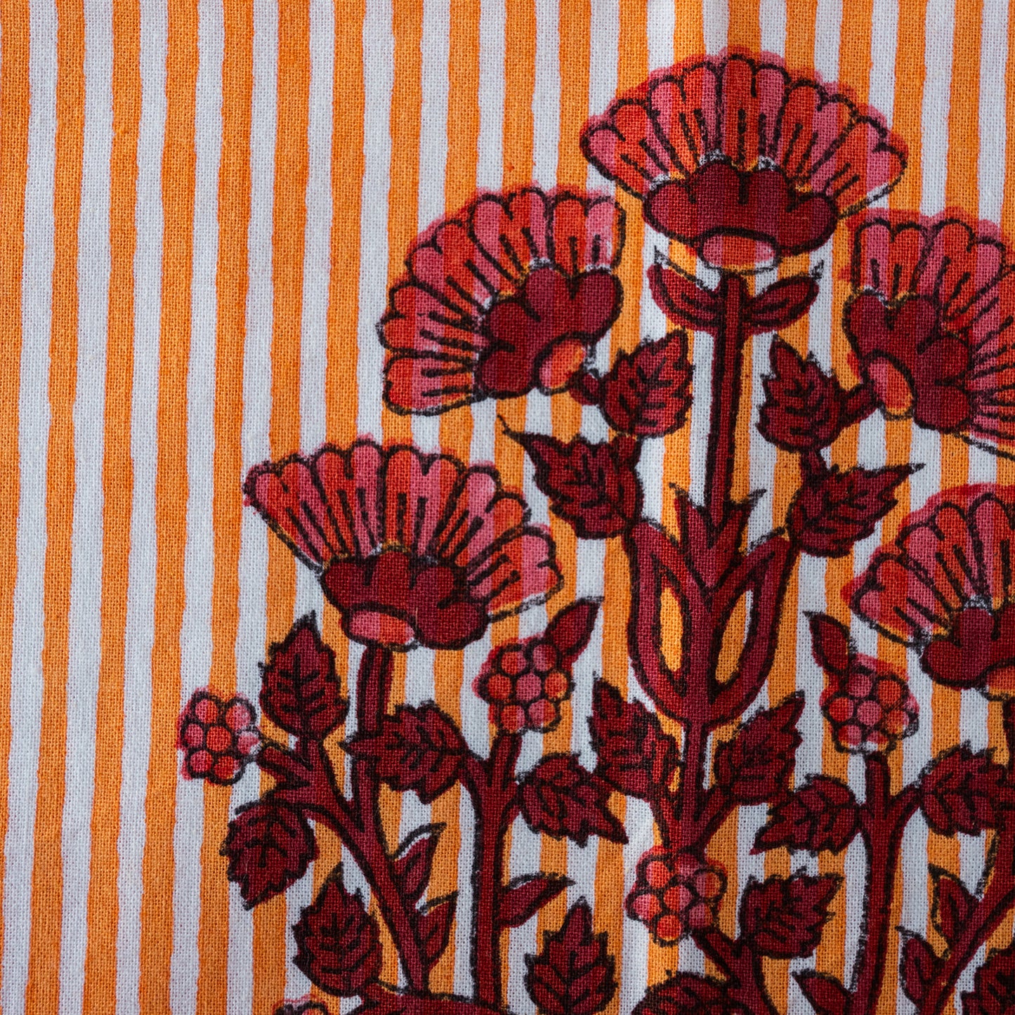 A close-up of a patterned textile featuring bold red and pink floral motifs over a white and orange striped background.