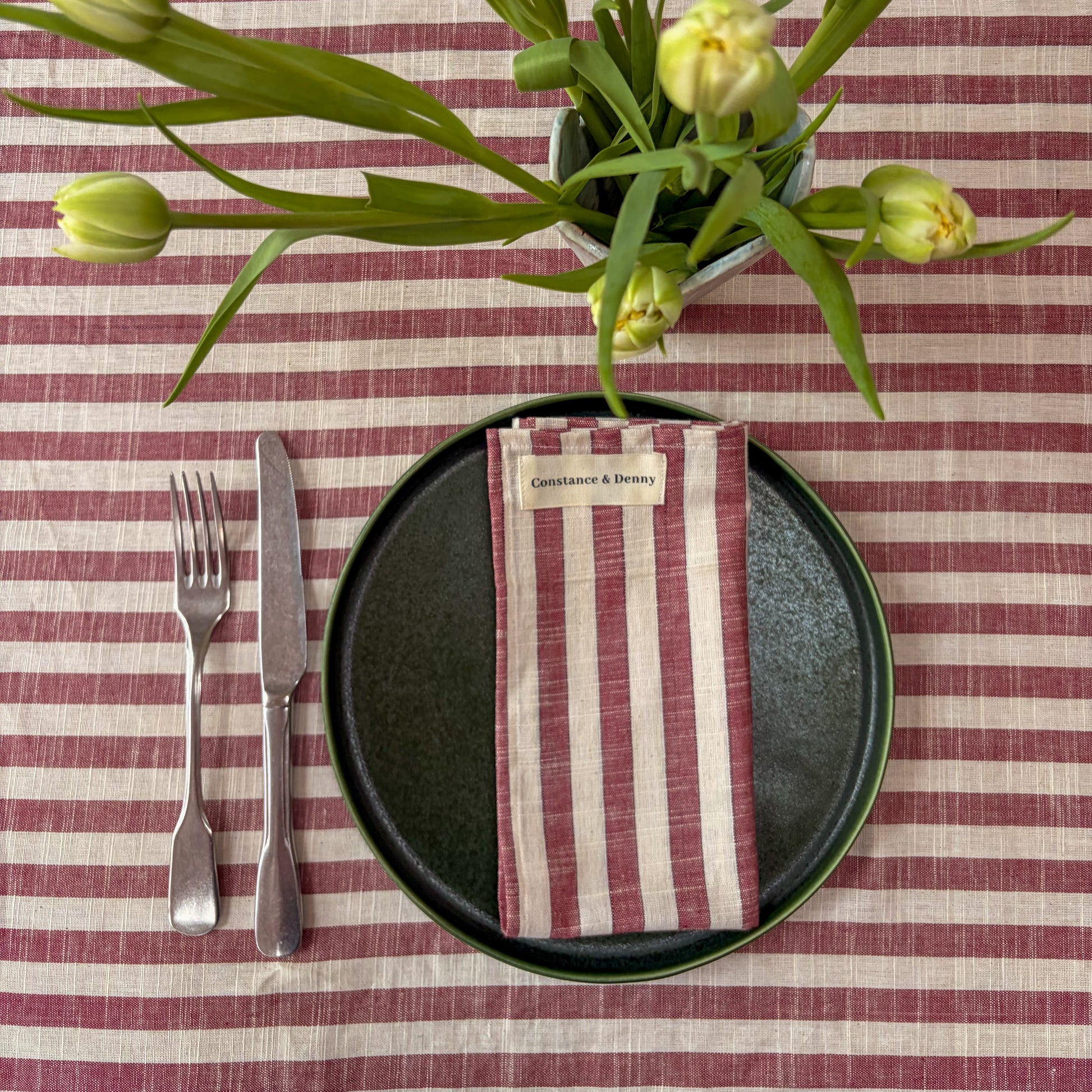 Table setting with a striped tablecloth, black plate, red and white striped napkin, and floral centerpiece.