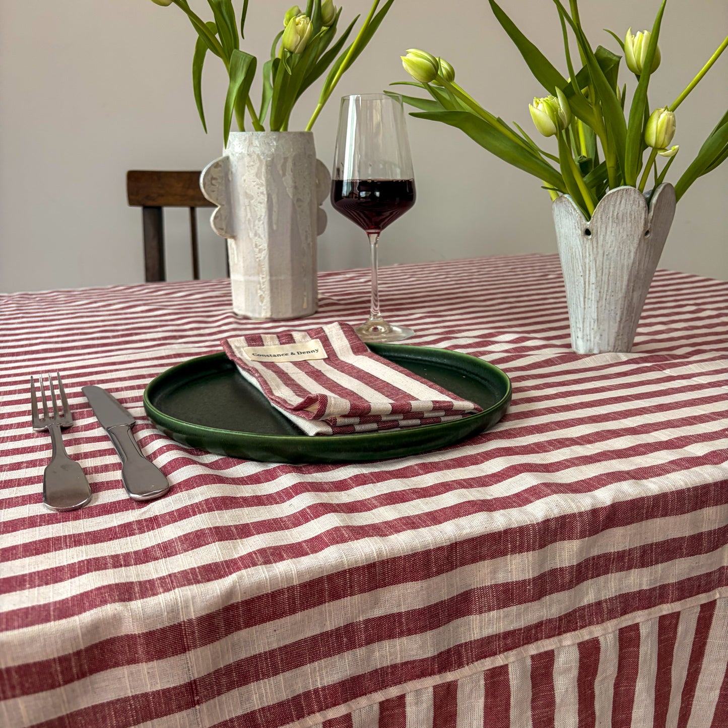 Dining table setting with striped tablecloth, floral arrangements, and wine glass.