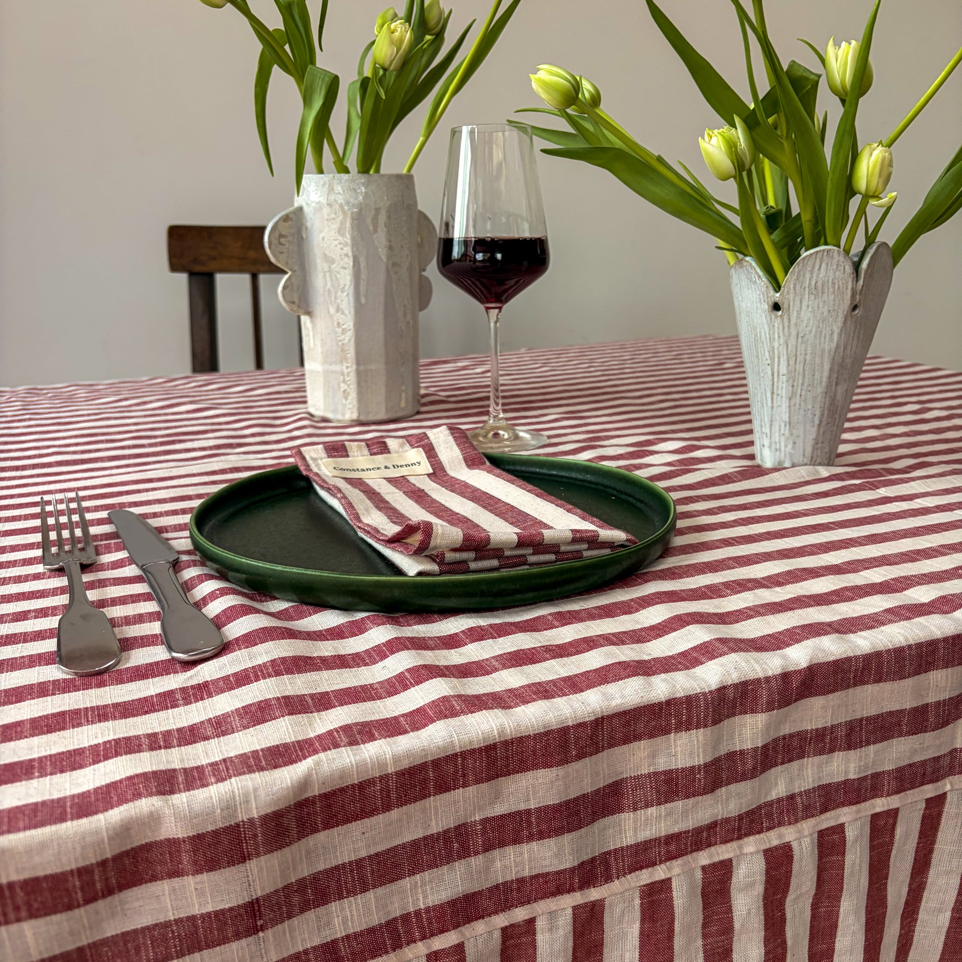 Dining table setting with striped tablecloth, floral arrangements, and wine glass.