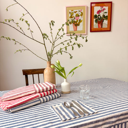 Dining table setting with striped tablecloth, red and white striped napkins, and framed pictures on the wall.