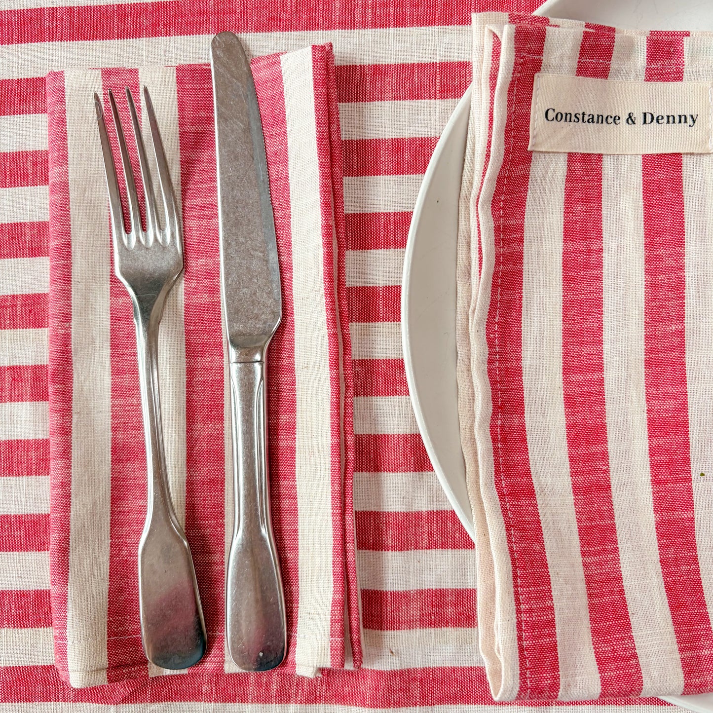 Silverware set on a red and white striped tablecloth with a branded napkin.